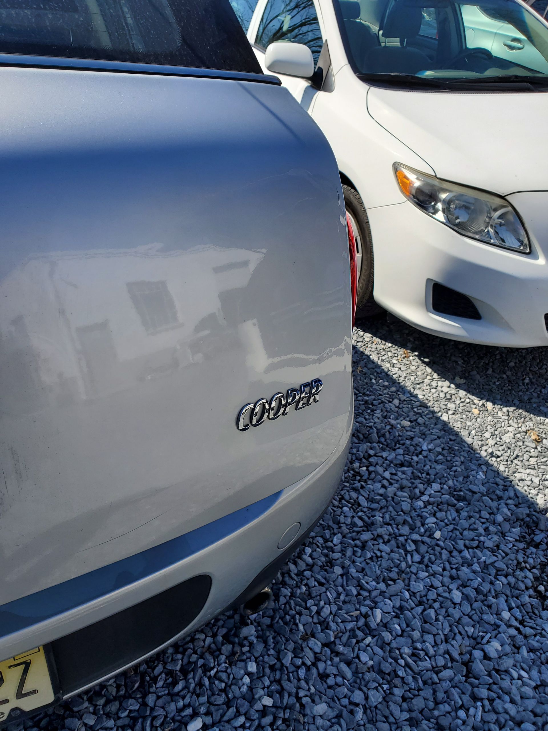 Two parked white cars on gravel, one close-up on the rear badge and license plate area.