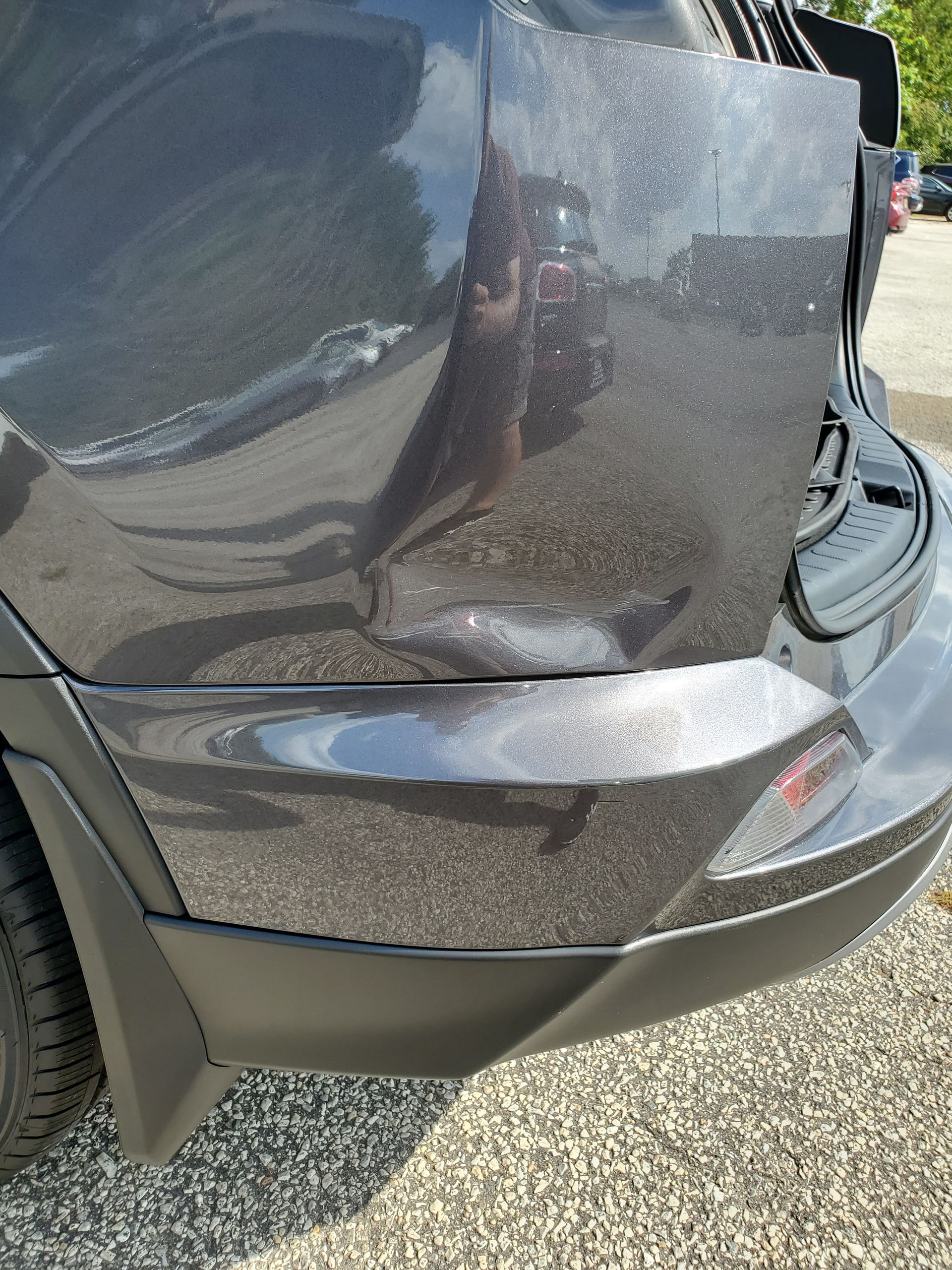 Close-up of a dark car’s rear side panel with a dent and scrape damage near the bumper.