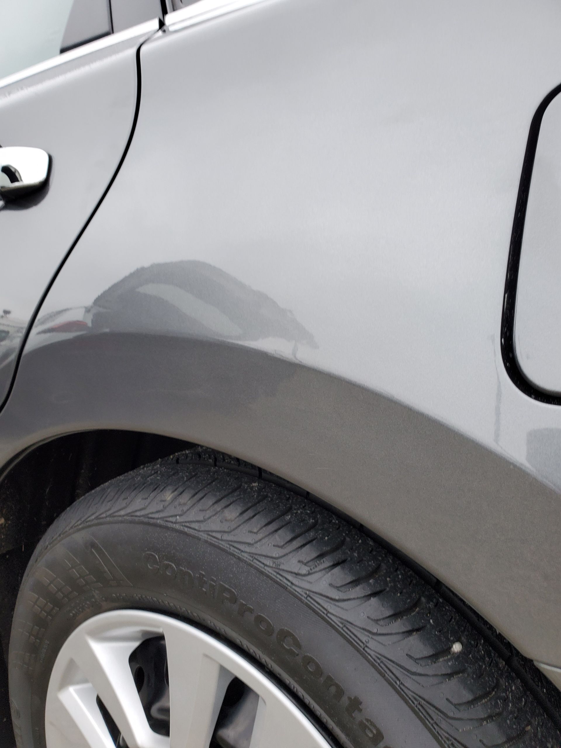 Gray car rear wheel and fender close-up with a dent above the wheel