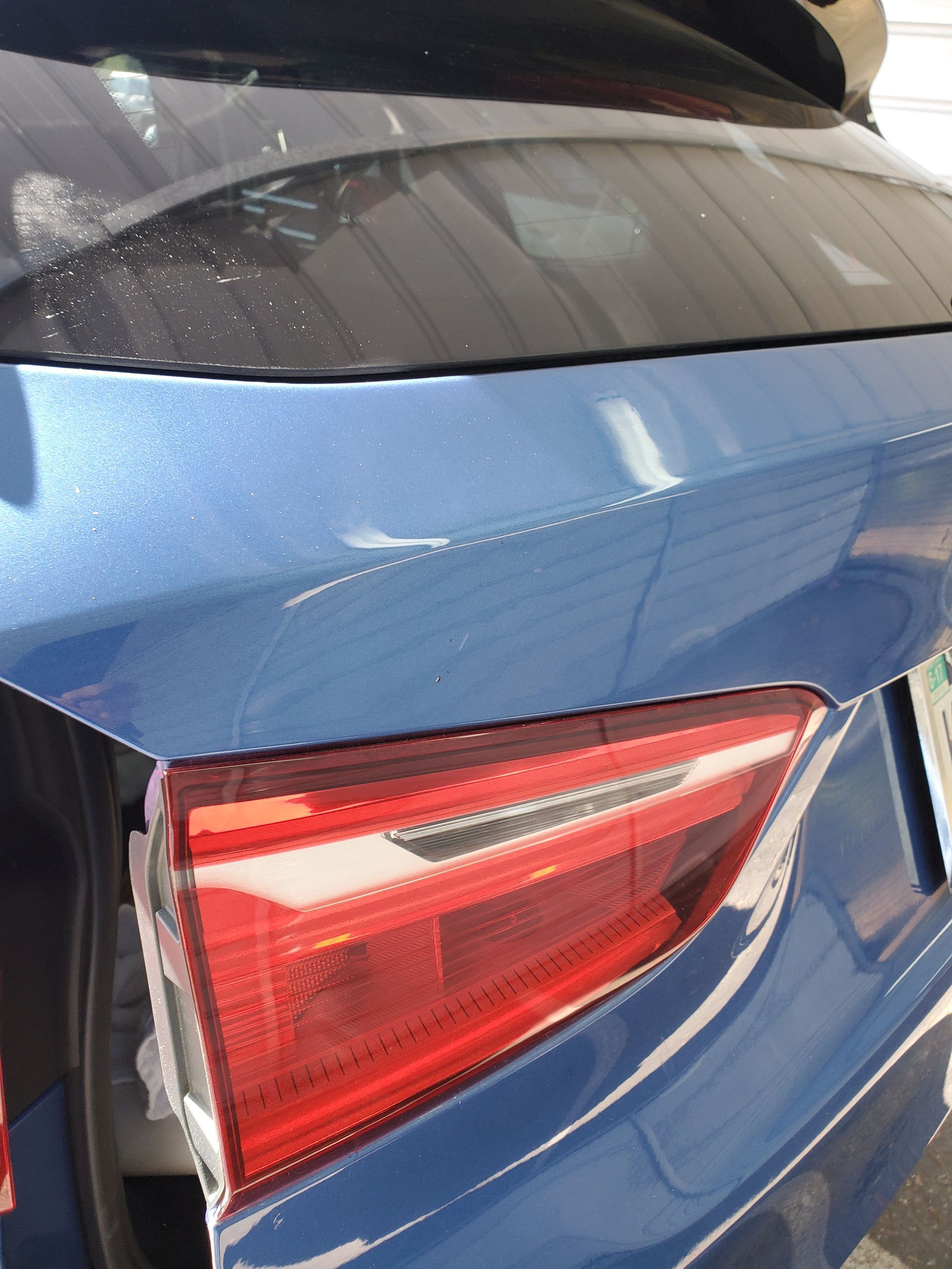 Close-up of a blue car’s rear taillight with a damaged bumper area