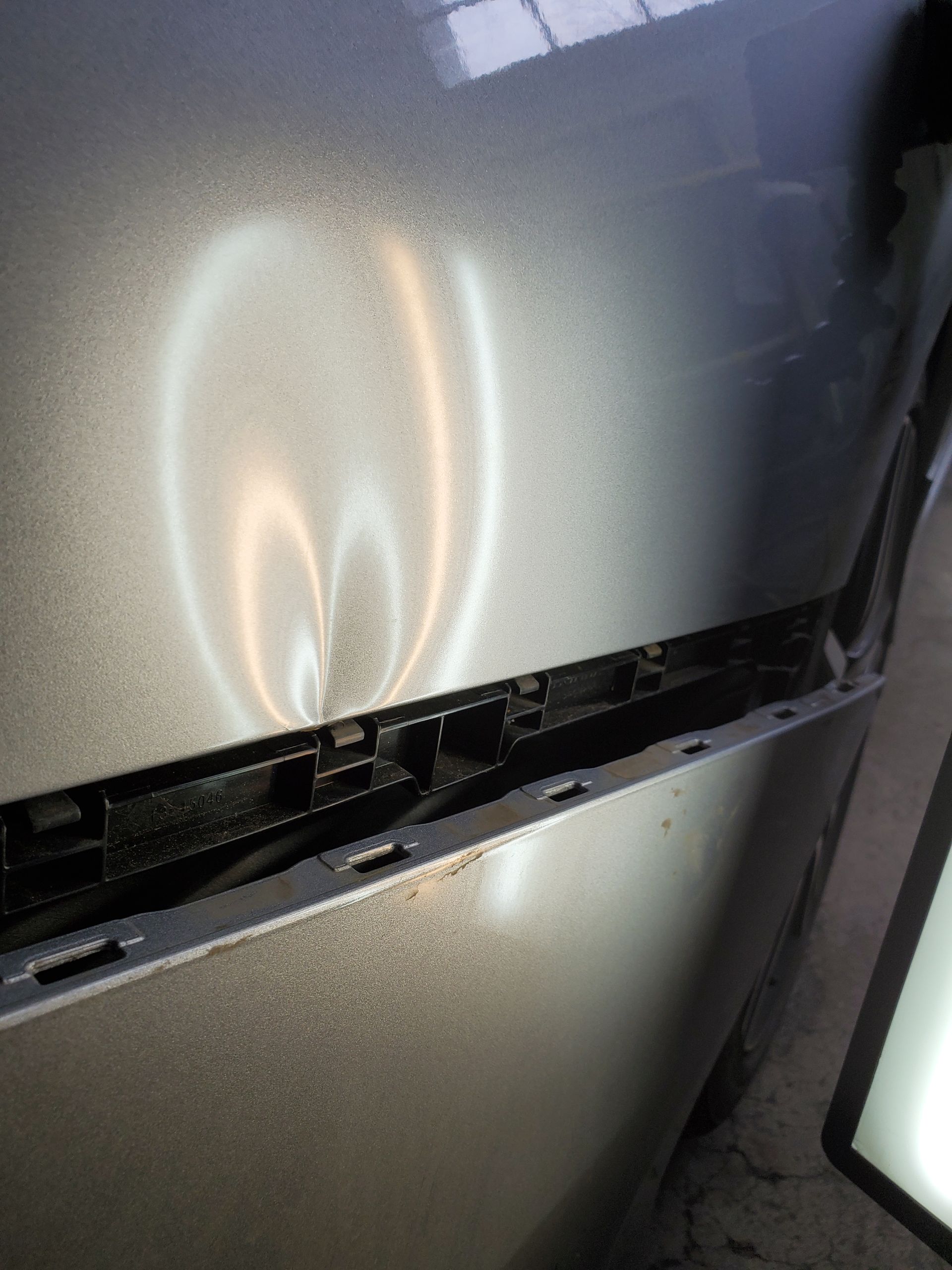 Damaged silver refrigerator door with a horizontal crack and dark broken section near the bottom
