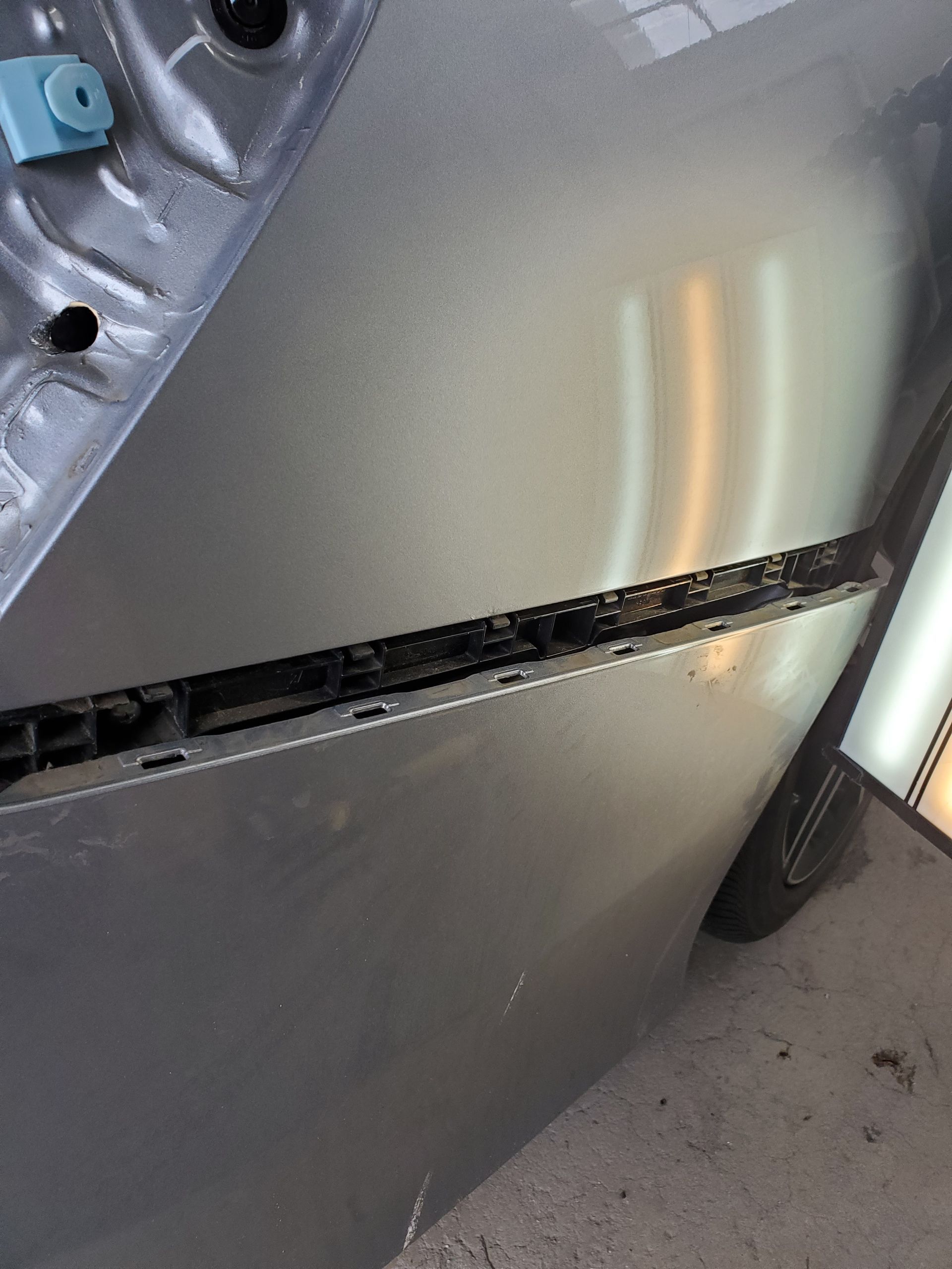 Close-up of a gray car door with a long horizontal dent and scratch near the lower panel
