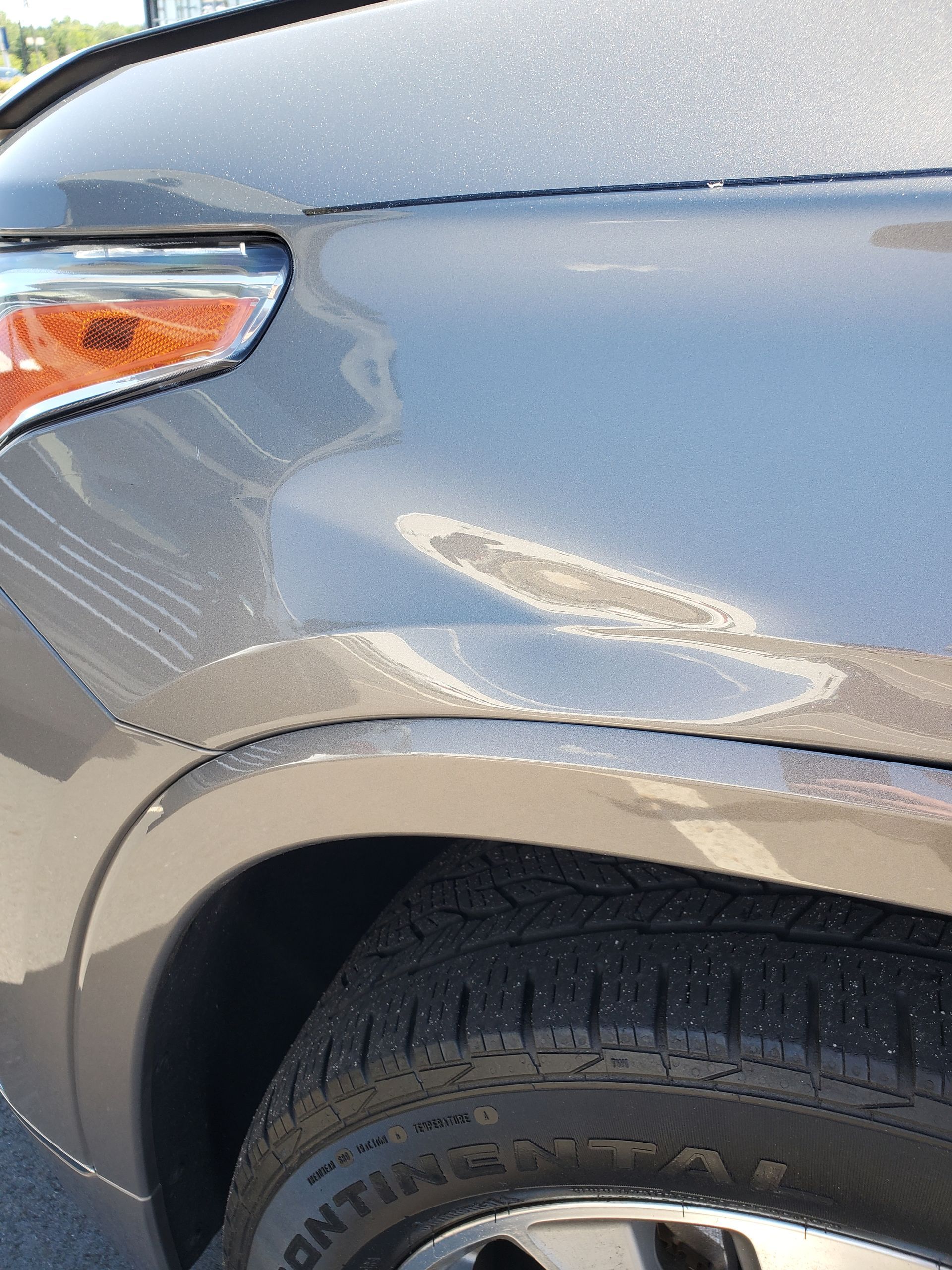 Close-up of a silver car’s front side panel with a dent above the wheel well