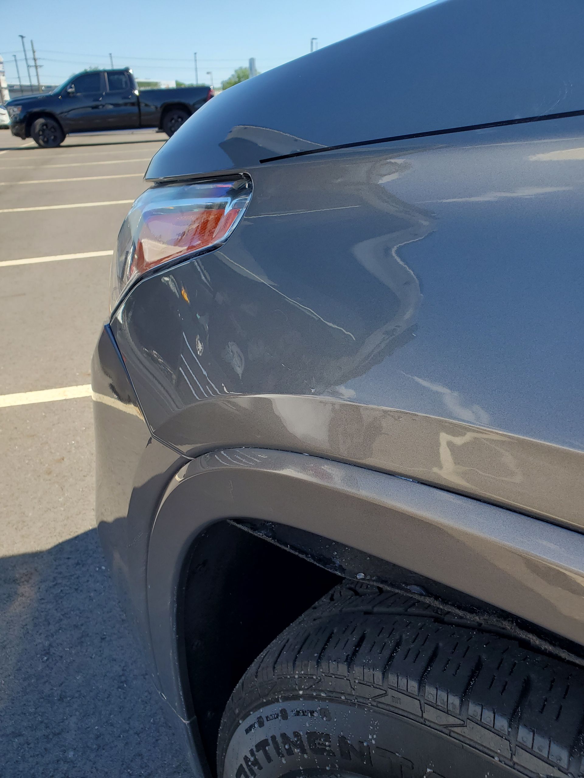 Close-up of a gray SUV’s front fender with a dent and scrapes in a parking lot