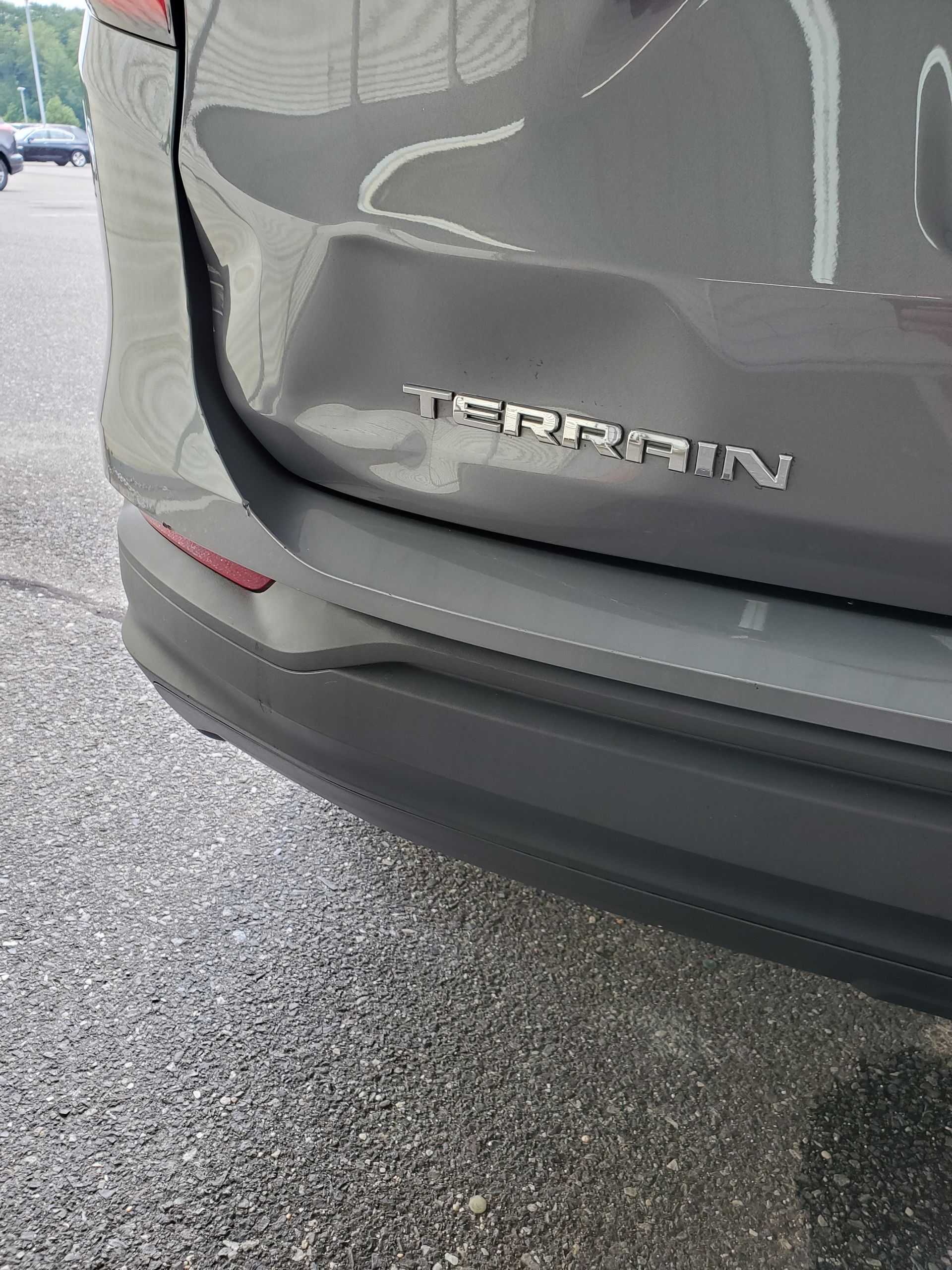 Close-up of the rear of a gray GMC Terrain SUV with a dented bumper on a wet parking lot.