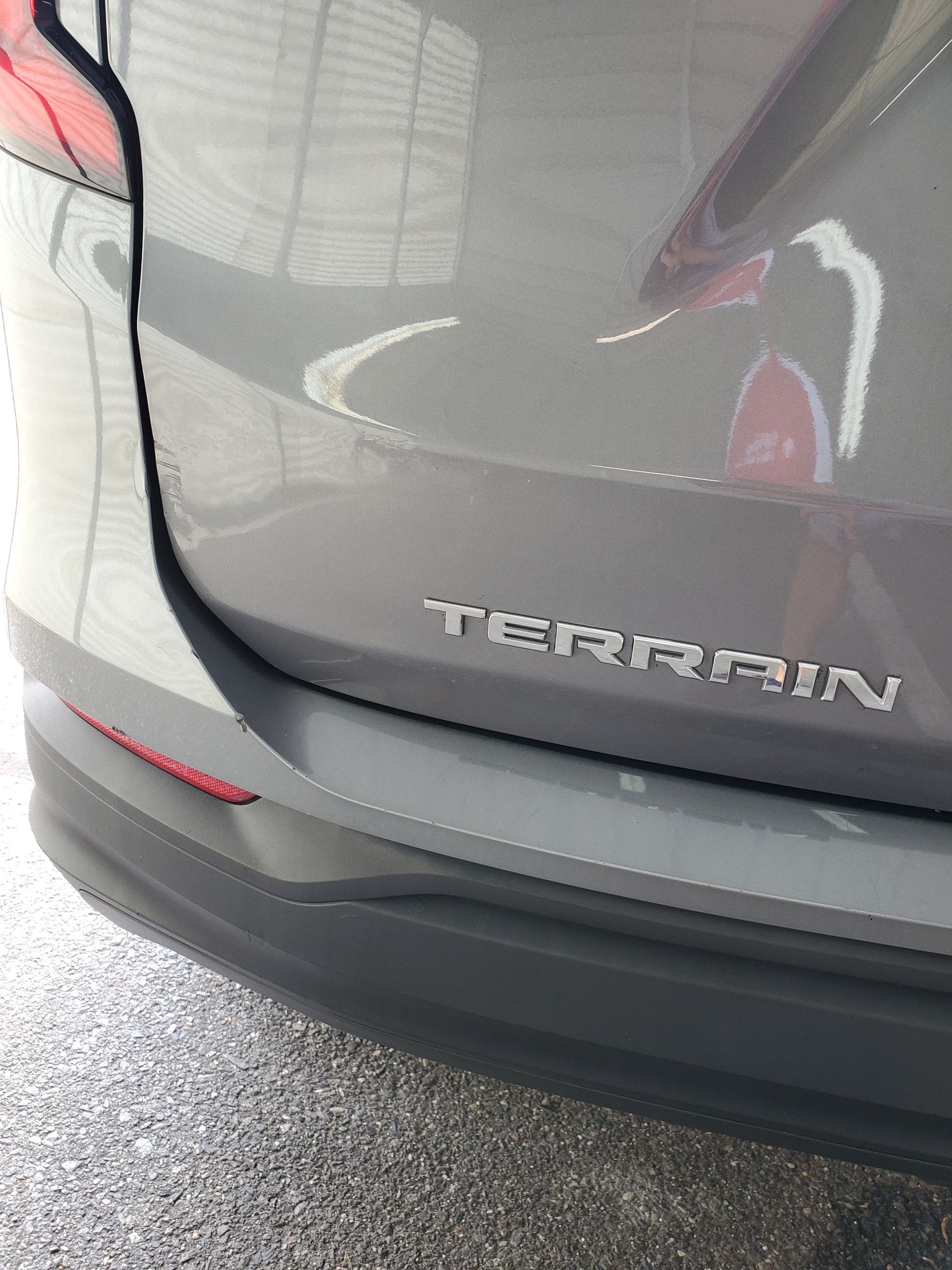 Rear of a gray Chevrolet Equinox with “Terrain” badge, parked close to a wet pavement.