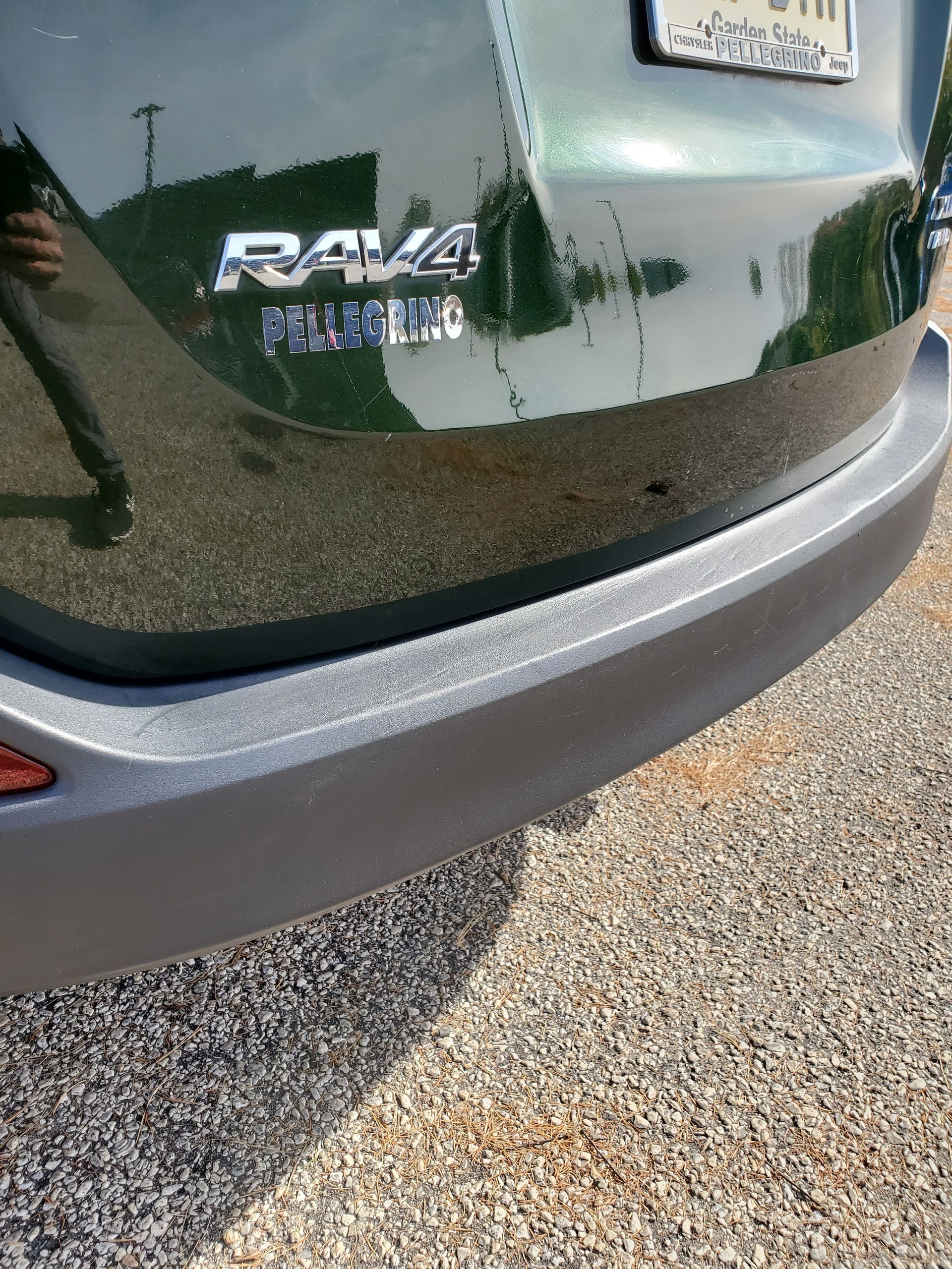 Rear of a dark green Toyota RAV4 with a silver bumper, parked on gravel.