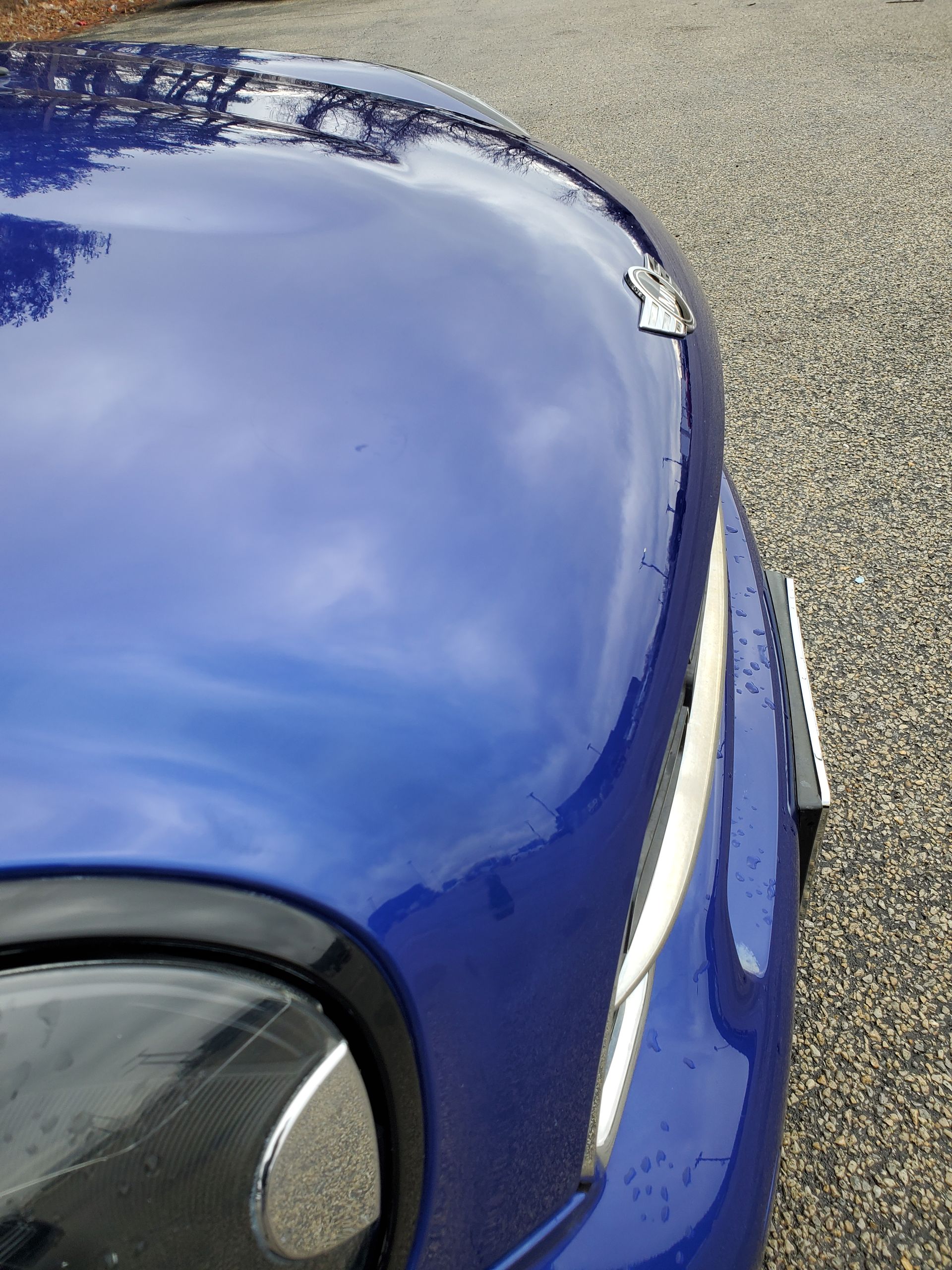 Close-up of a blue car hood and headlight on a gravel road
