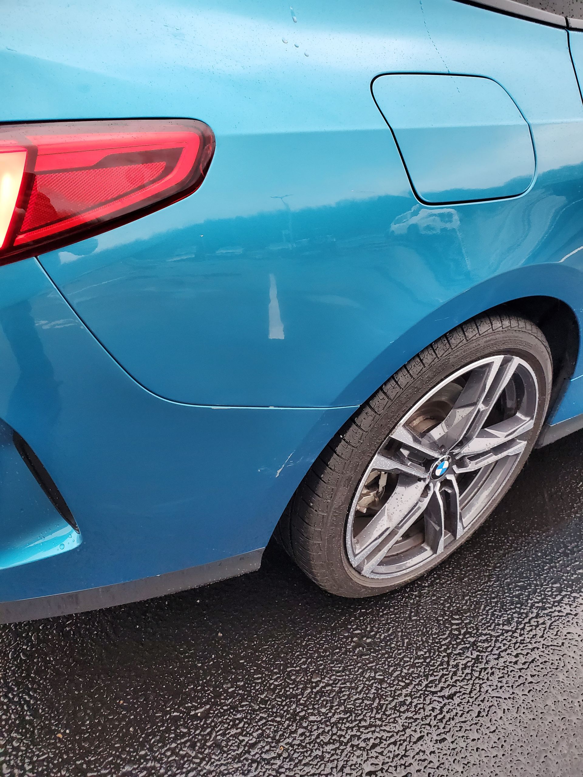Blue car rear quarter panel with wheel and fuel door on a wet street