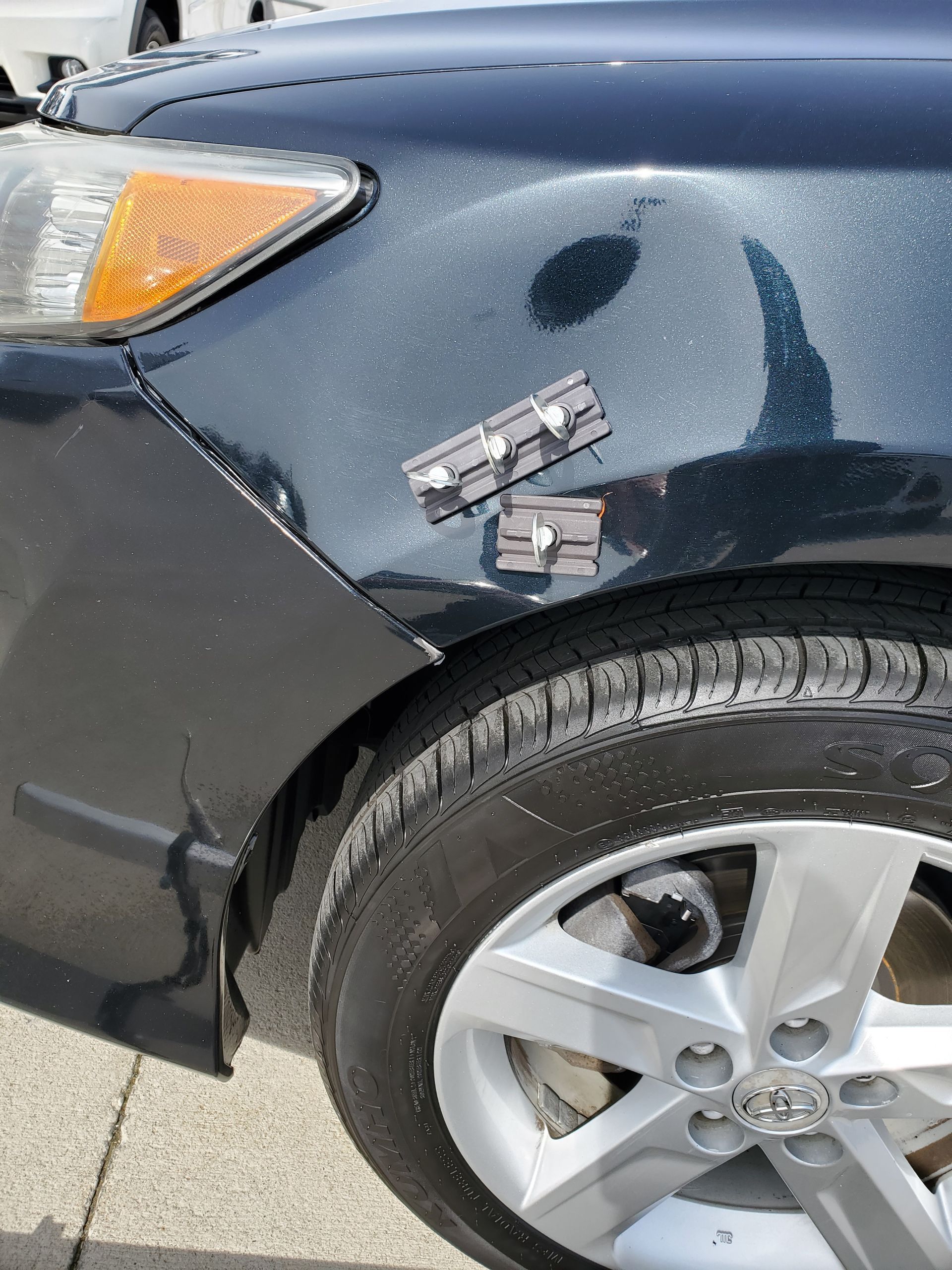 Black car front fender with dent and tape, close-up of damaged wheel arch and tire