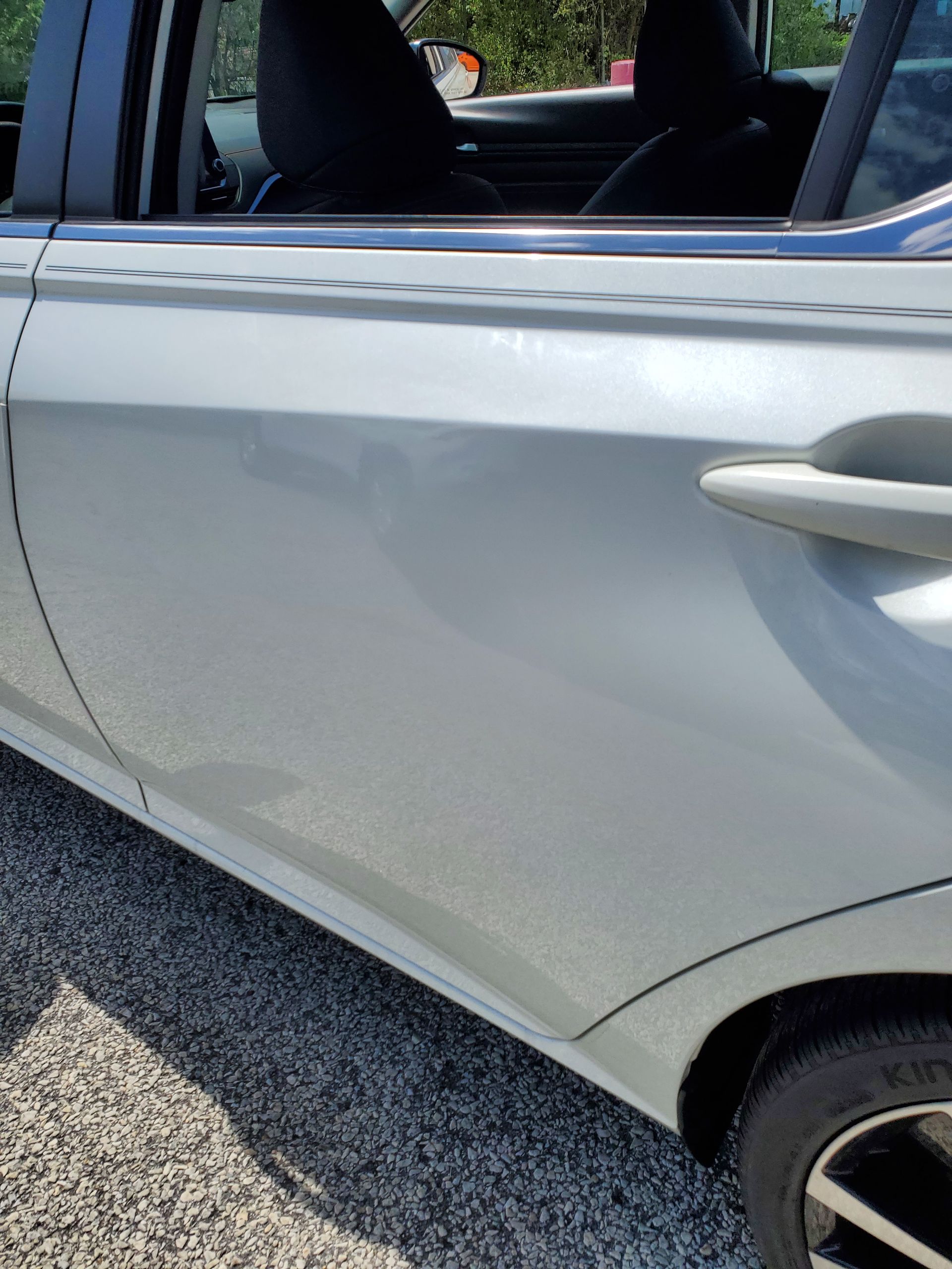 Close-up of a silver car door with a visible dent and scuff near the lower panel