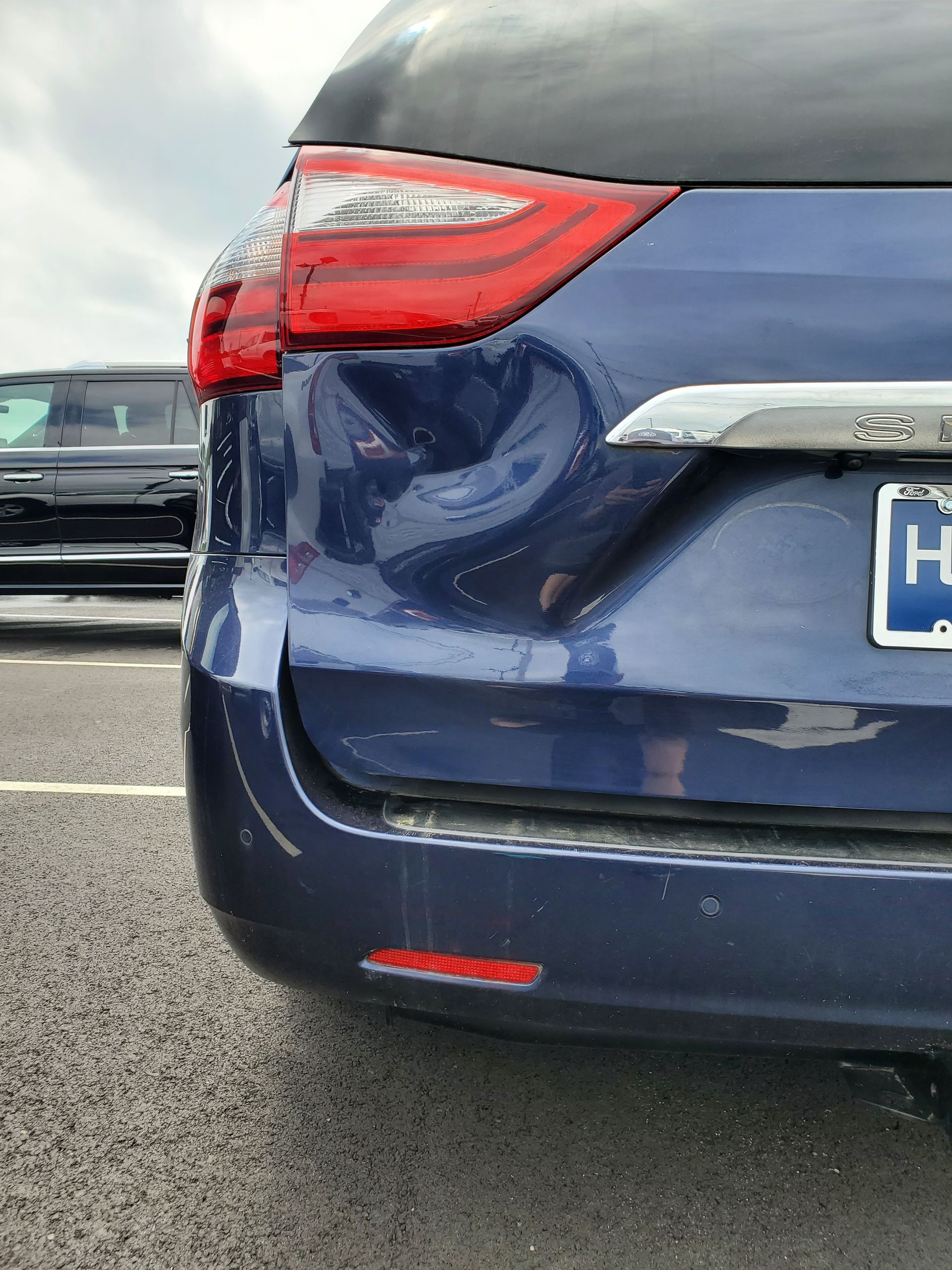 Rear view of a blue car with a damaged rear bumper in a parking lot
