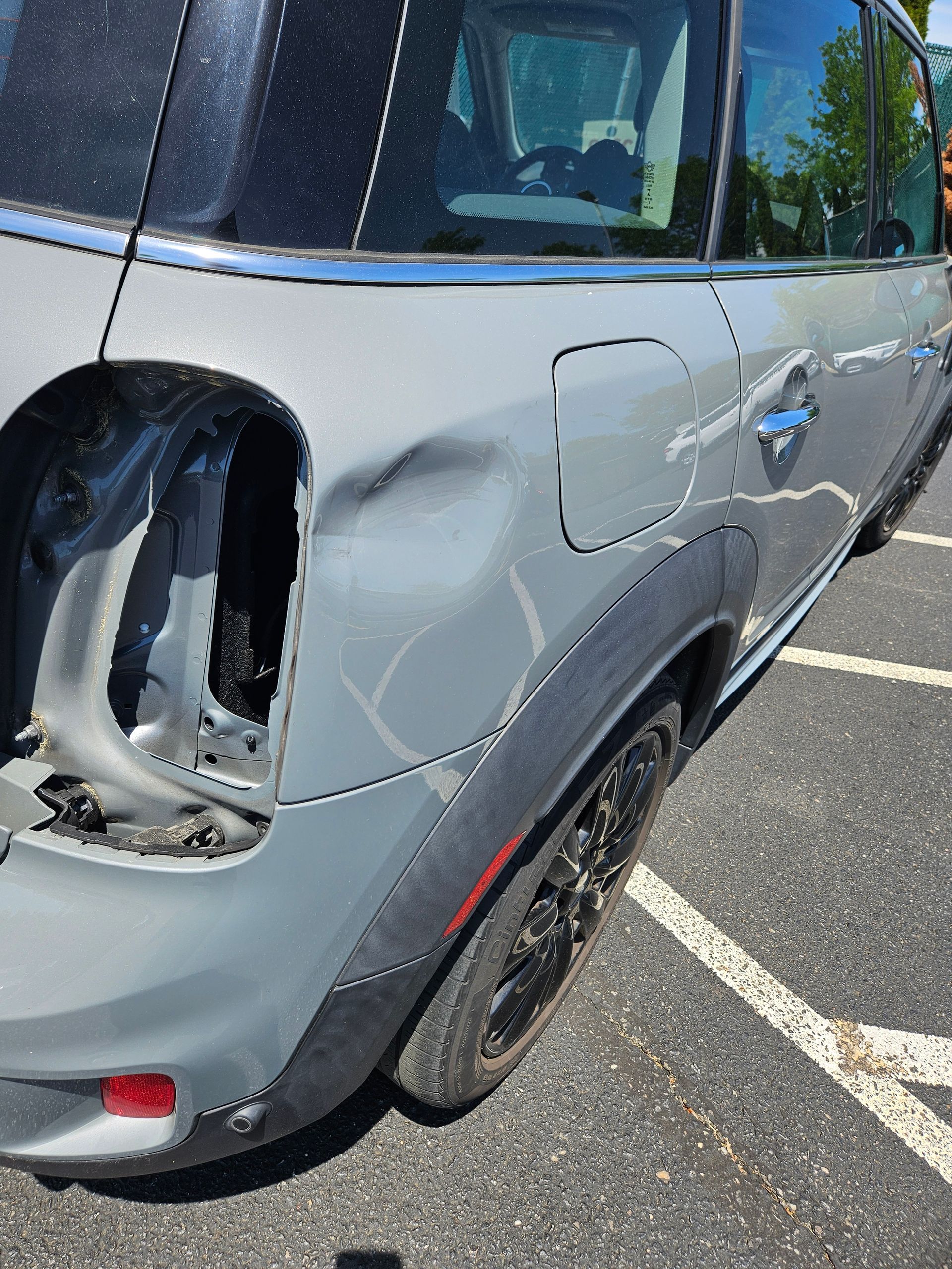 Gray SUV with rear left side damage and missing tail light in a parking lot