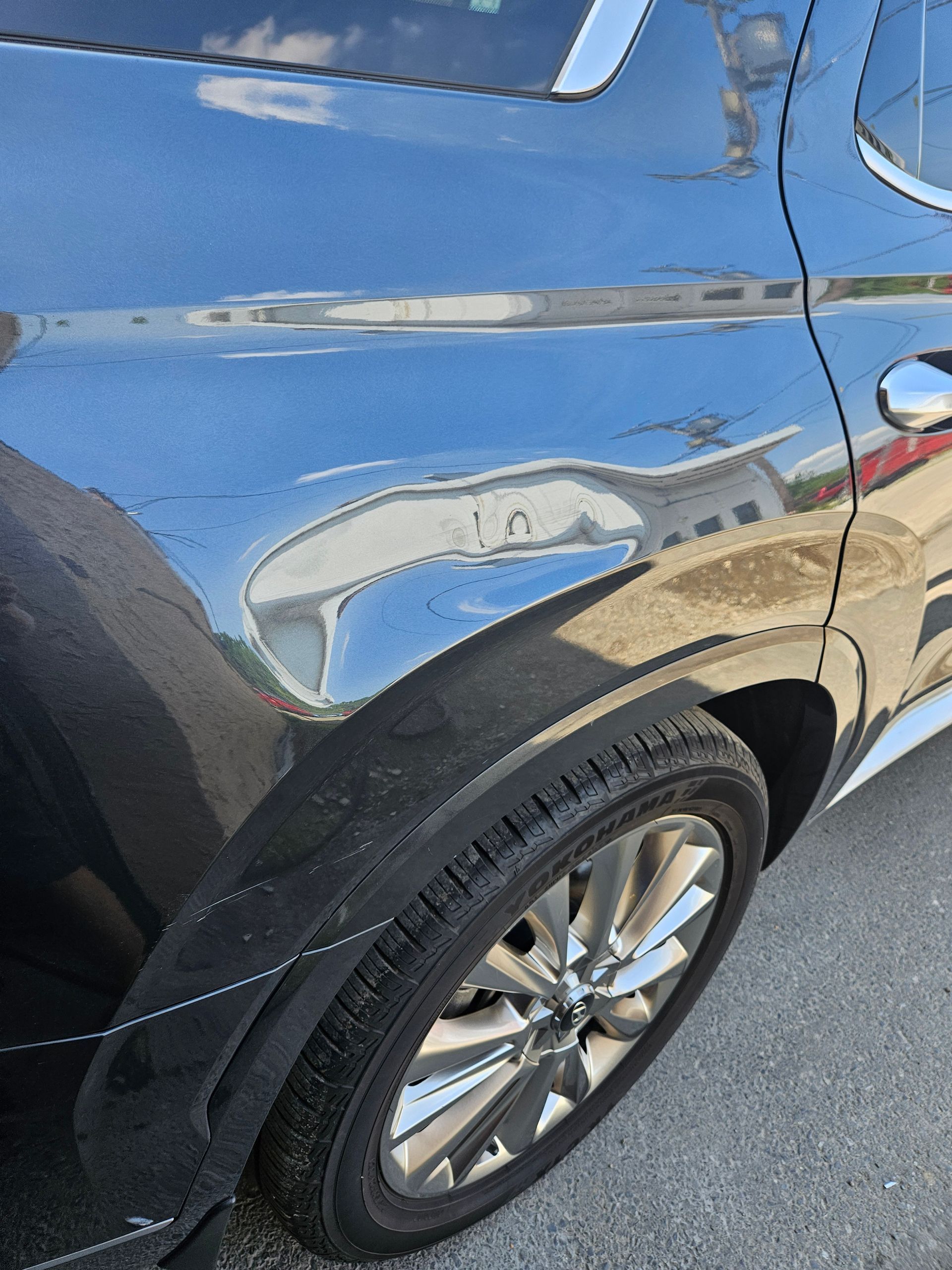 Blue SUV with a large dent and scrape on the rear passenger-side door above the wheel