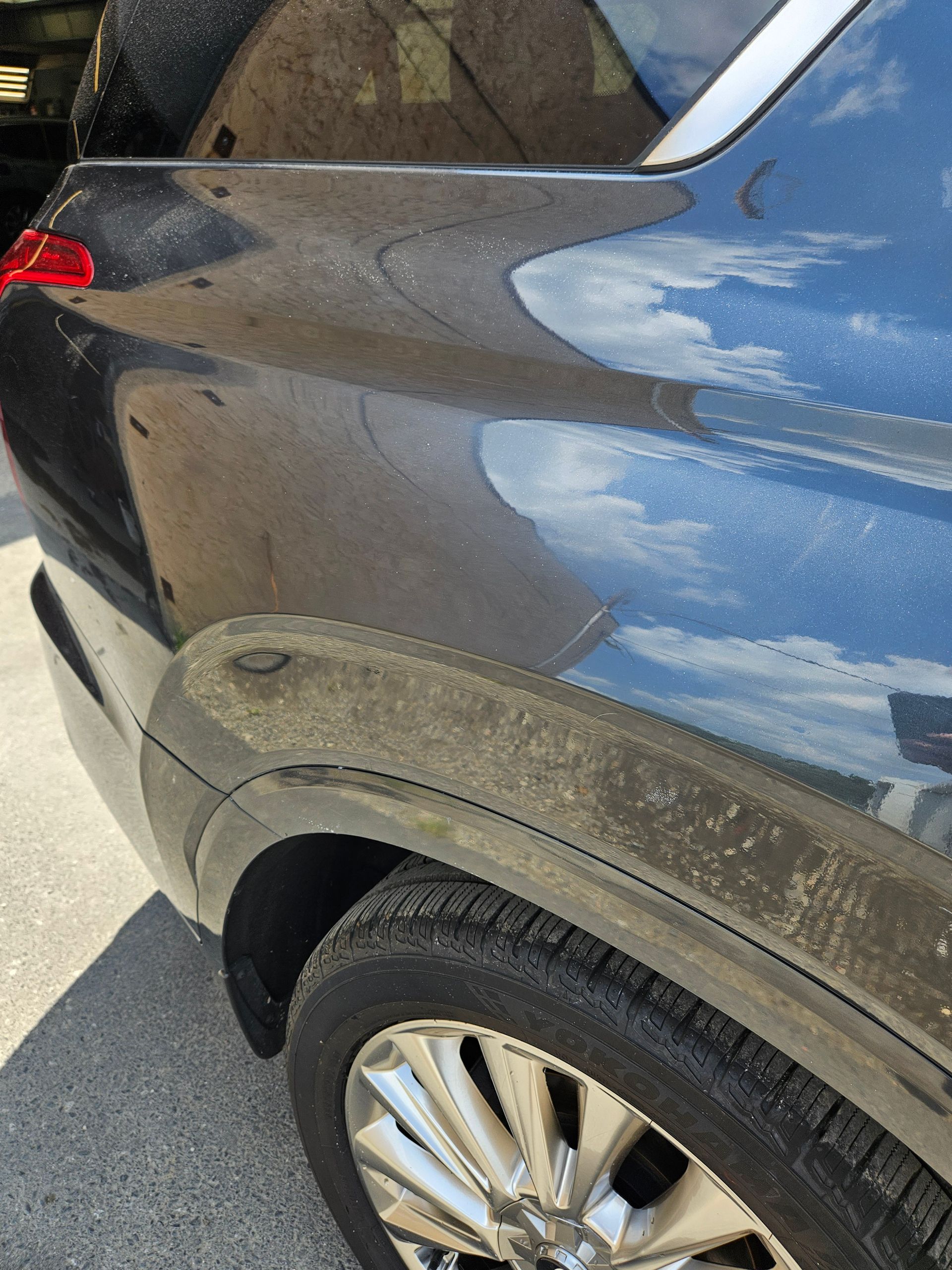 Close-up of a dark SUV’s rear quarter panel with a scuffed bumper and wheel visible.