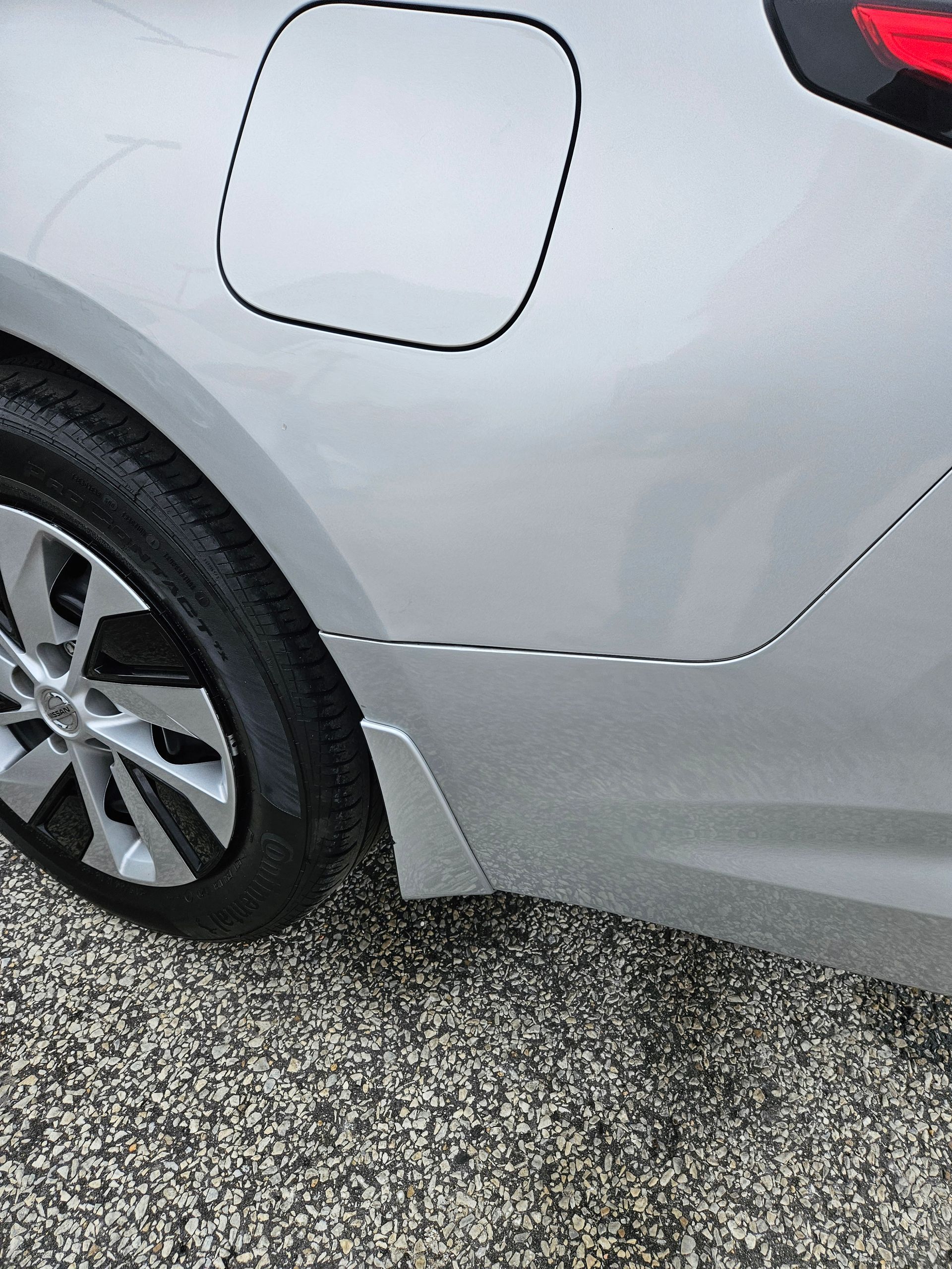 Rear side of a silver car with a visible fuel door and rear wheel.