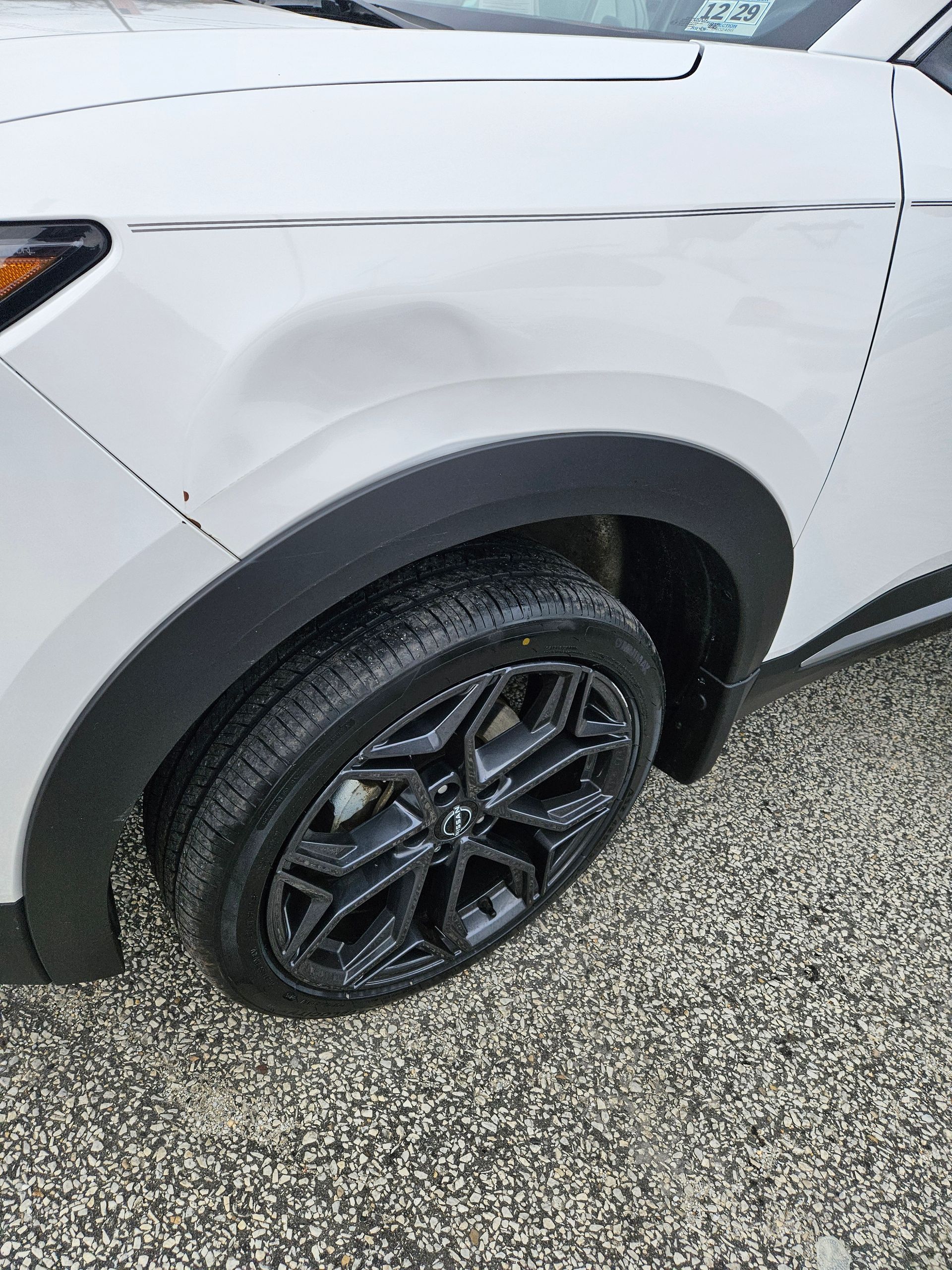 Close-up of a white SUV’s front wheel and fender with a black alloy rim on wet pavement
