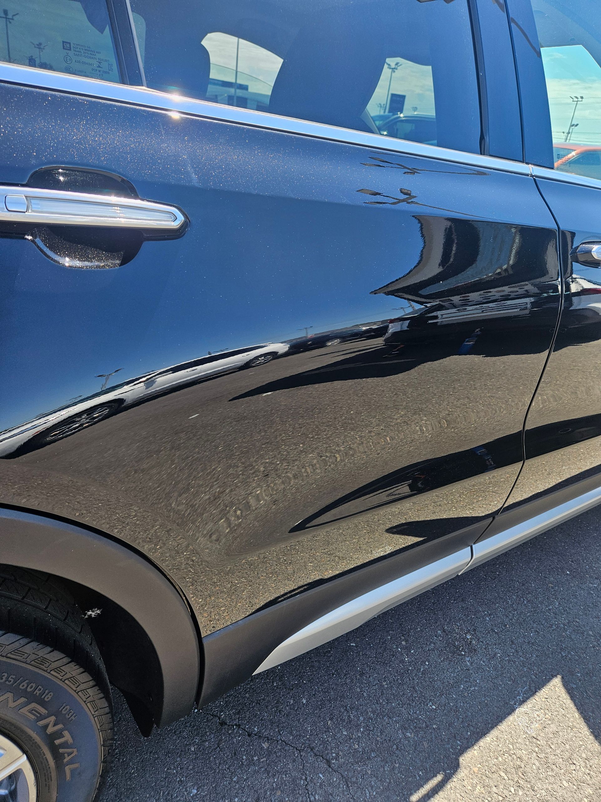 Black SUV side door with chrome handle and reflections, parked on pavement.