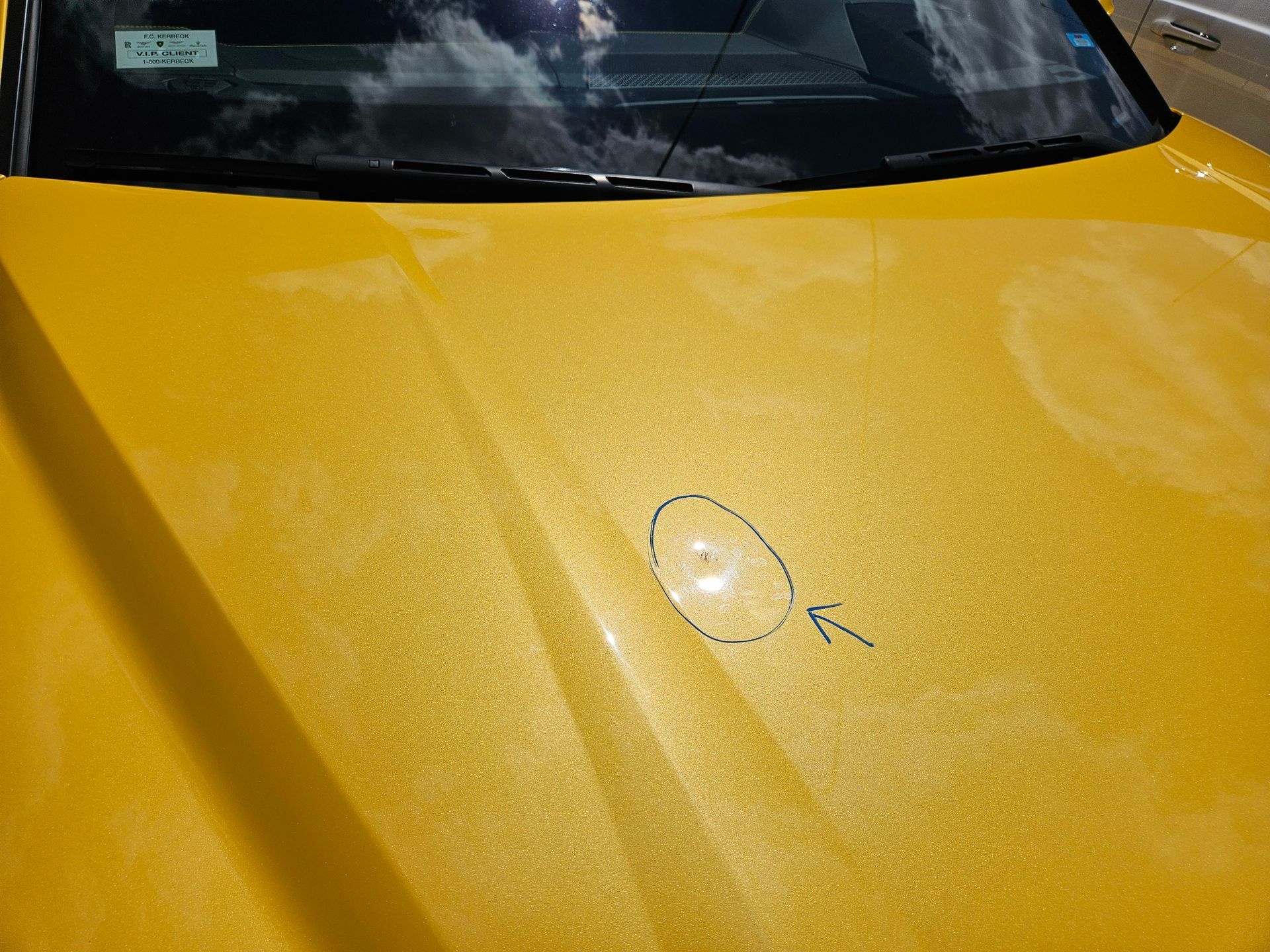 Yellow car hood with a small circular dent or paint mark near the center