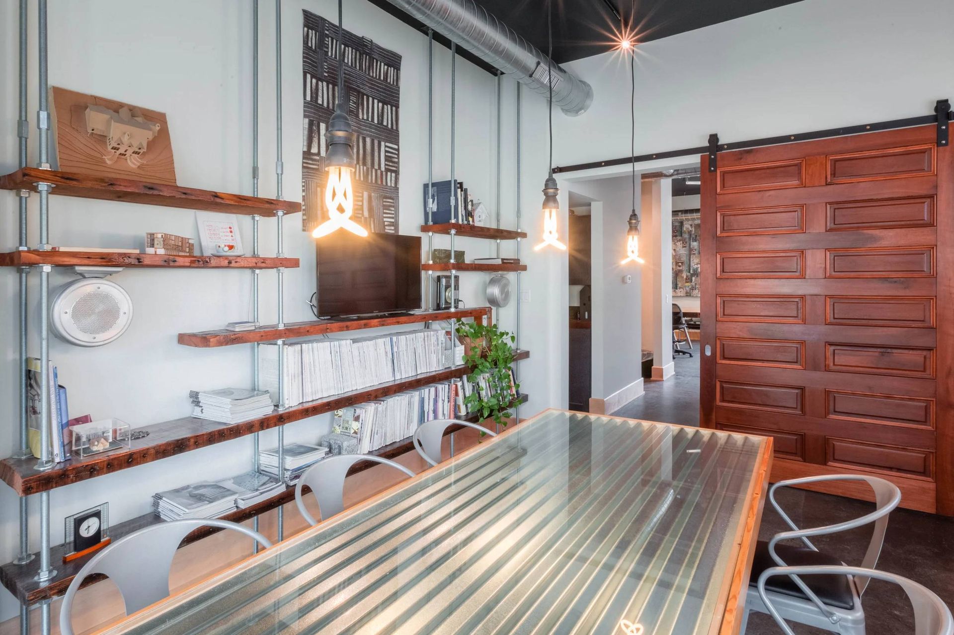 Modern industrial dining room with wooden table, metal shelving, and hanging pendant lights
