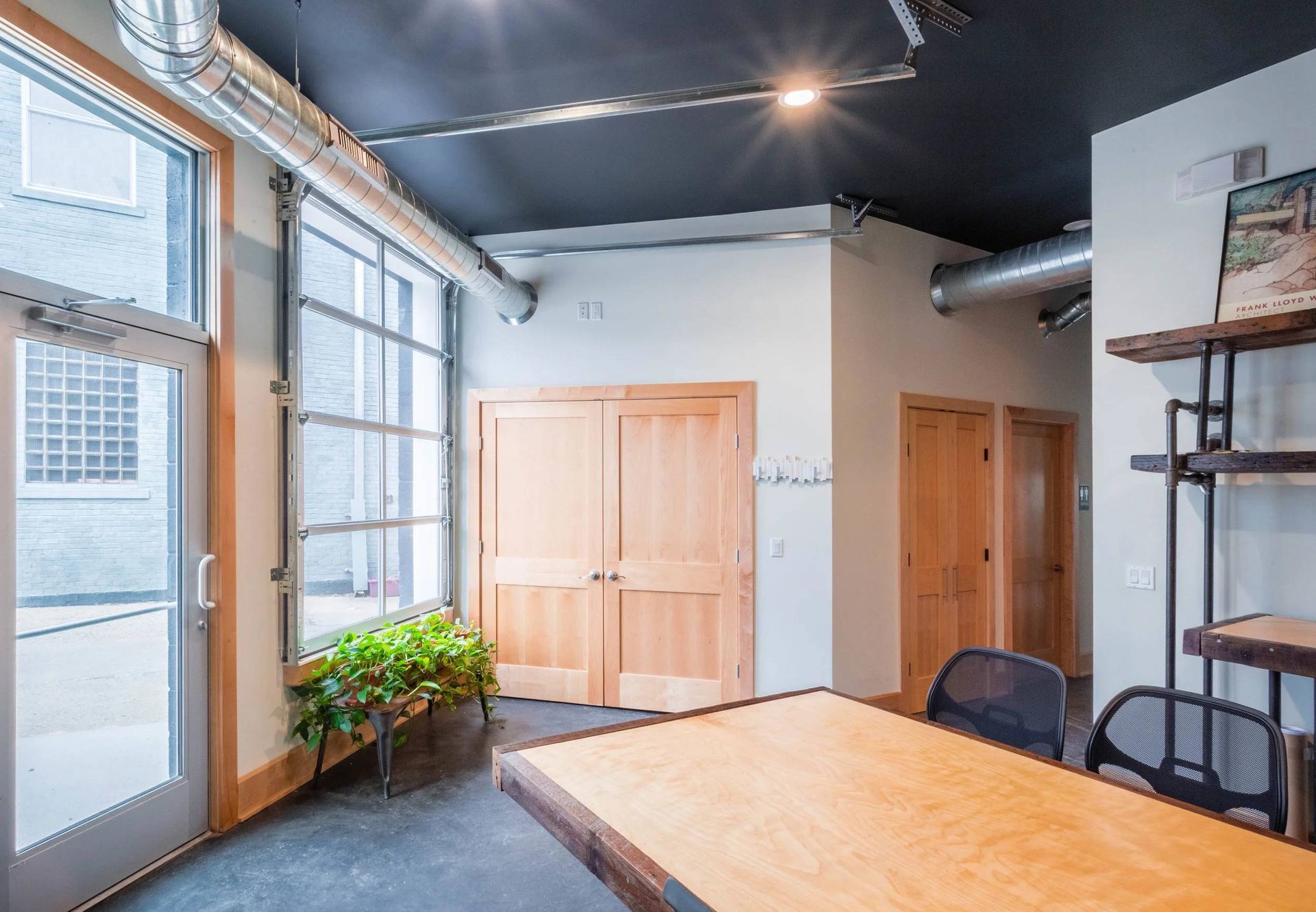 Modern office interior with large windows, wooden doors, a desk, and black ceiling beams