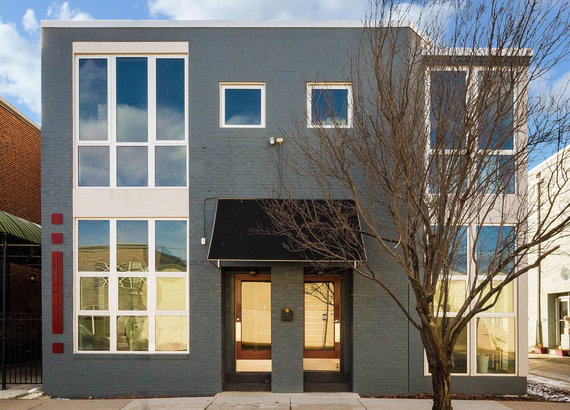 Modern two-story gray house with large windows and a leafless tree in front