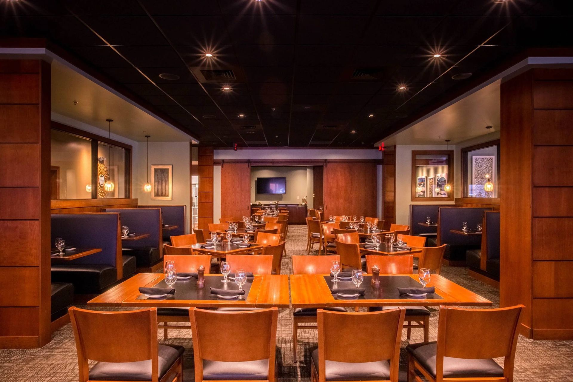 Empty upscale restaurant dining room with orange tables, leather chairs, and warm ceiling lights