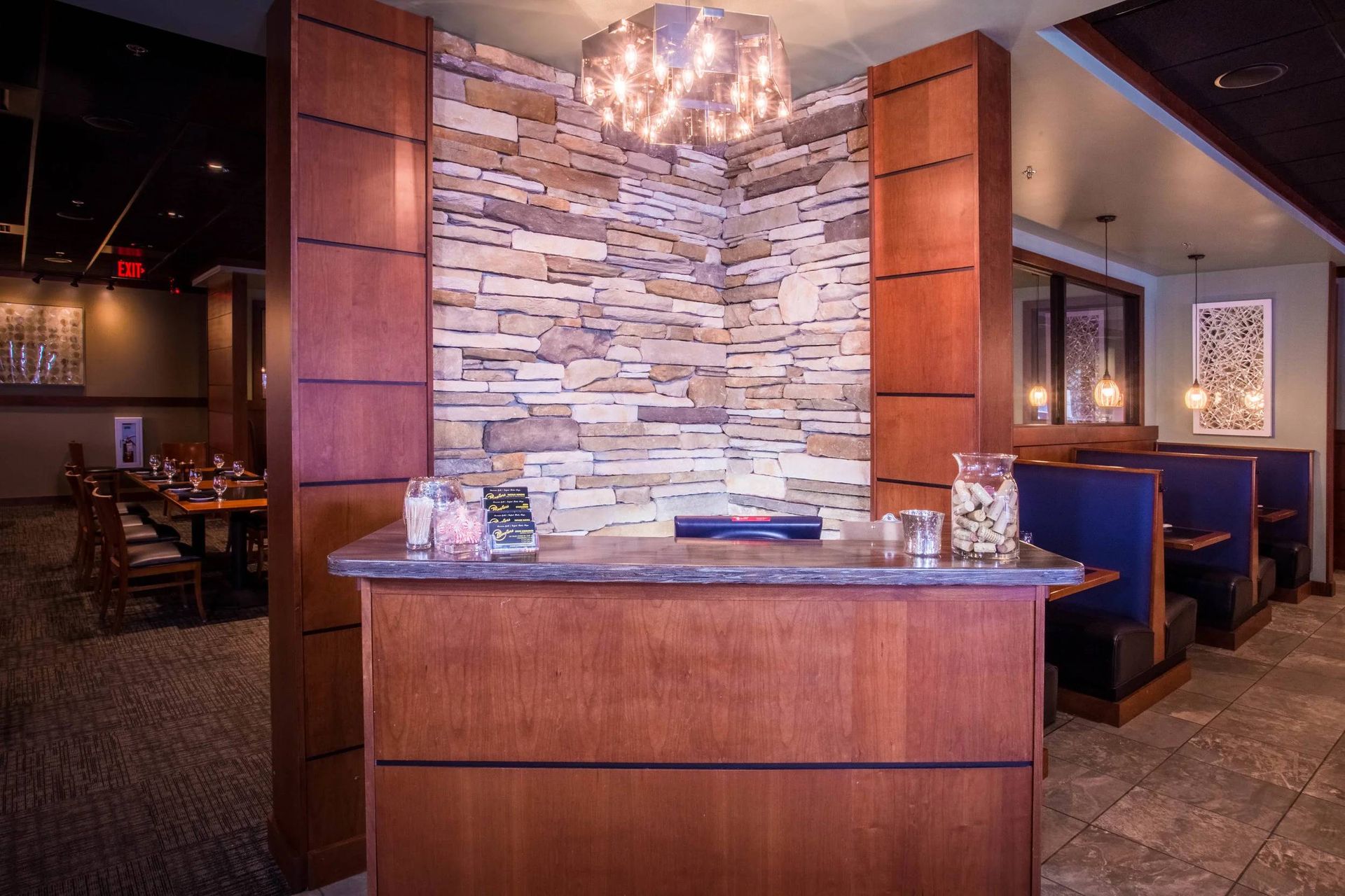 Restaurant host stand with stone accent wall, wood paneling, and blue booth seating nearby