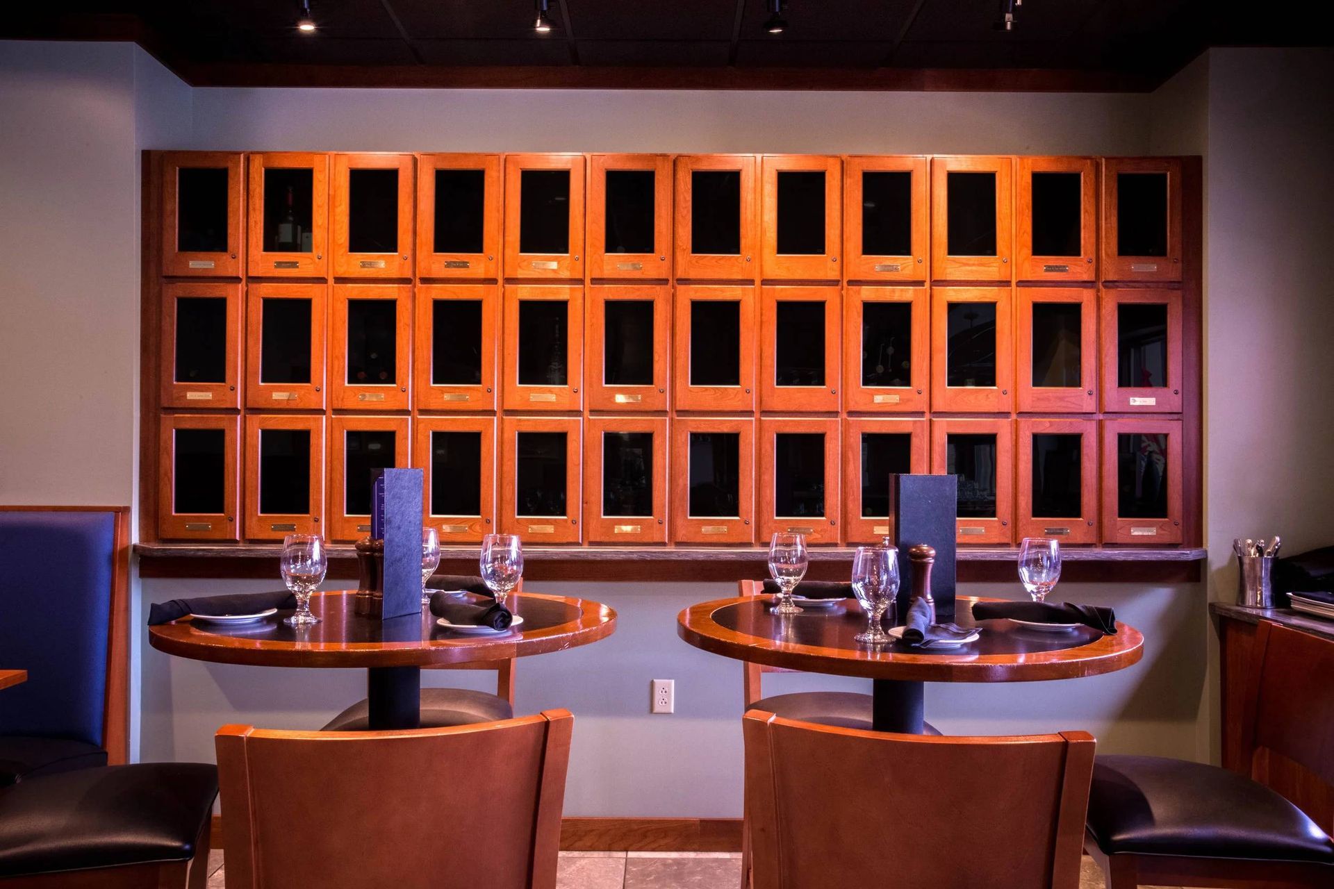 Dim restaurant interior with two set dining tables in front of a wall of small square windows
