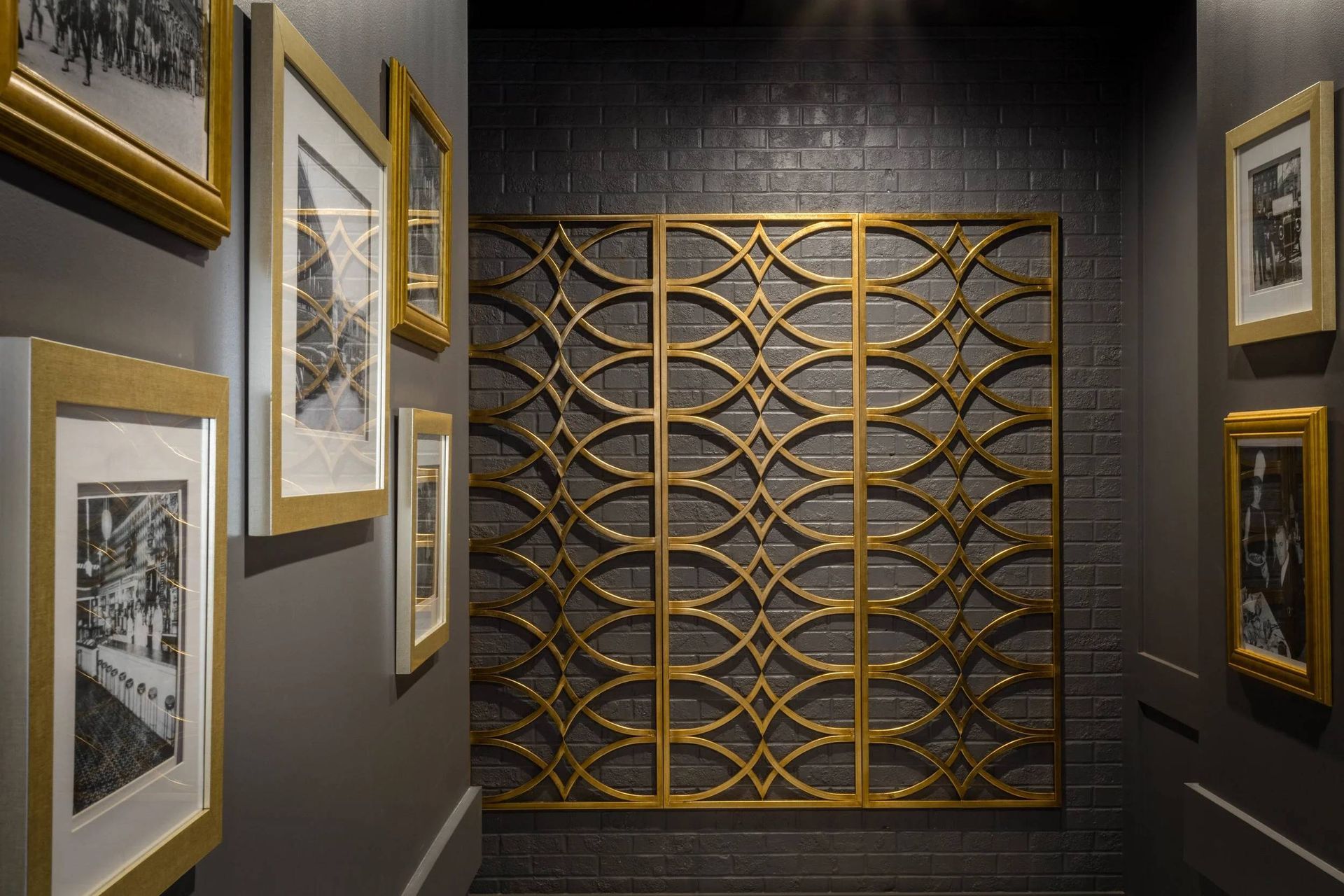 Art gallery hallway with framed black-and-white prints and a gold geometric wall sculpture on a dark wall
