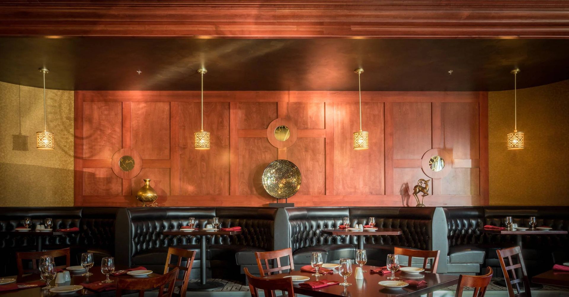 Empty modern restaurant interior with warm wood paneling, red chairs, and hanging pendant lights