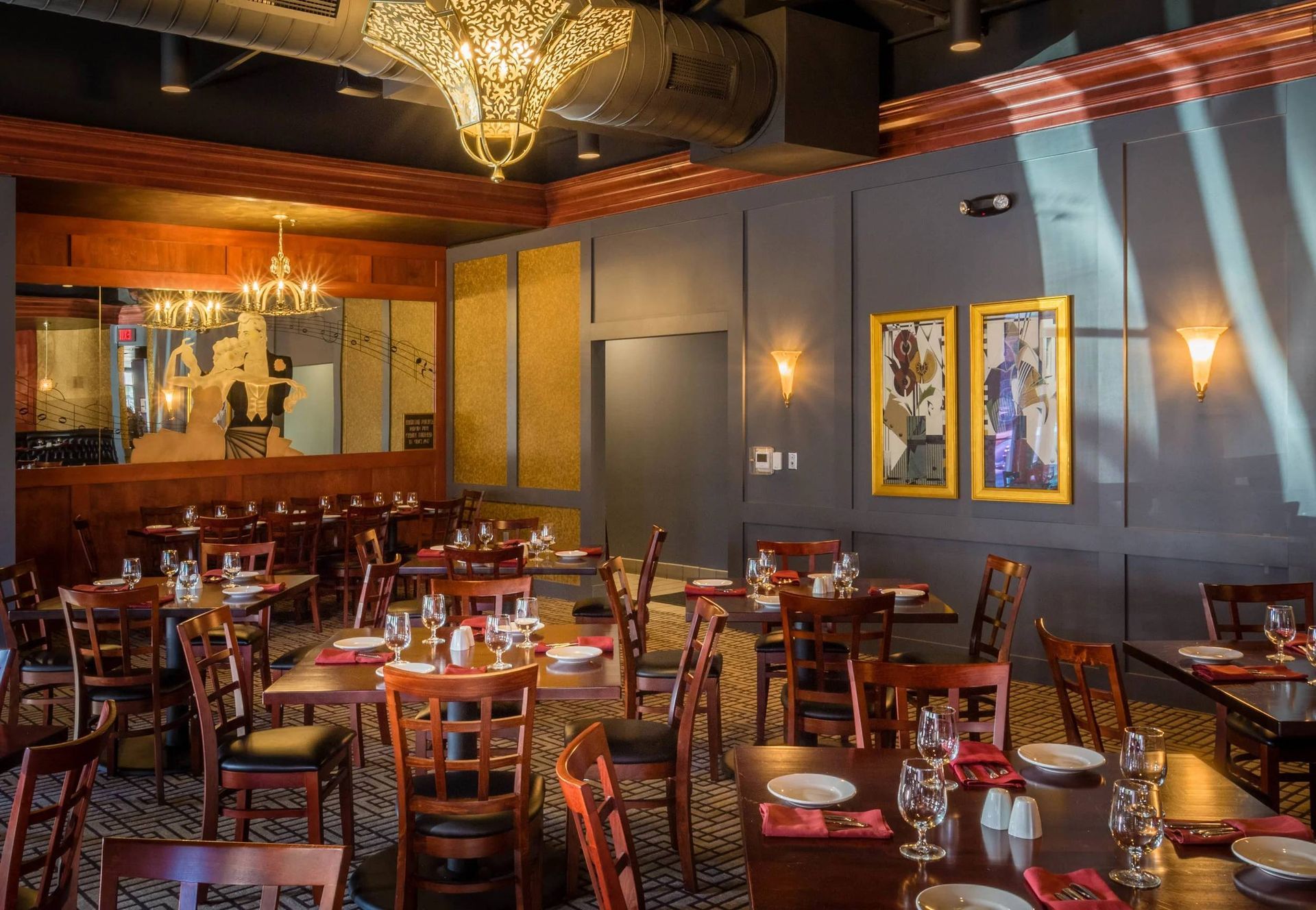 Warm restaurant dining room with wooden tables, red chairs, gold accents, and framed wall art