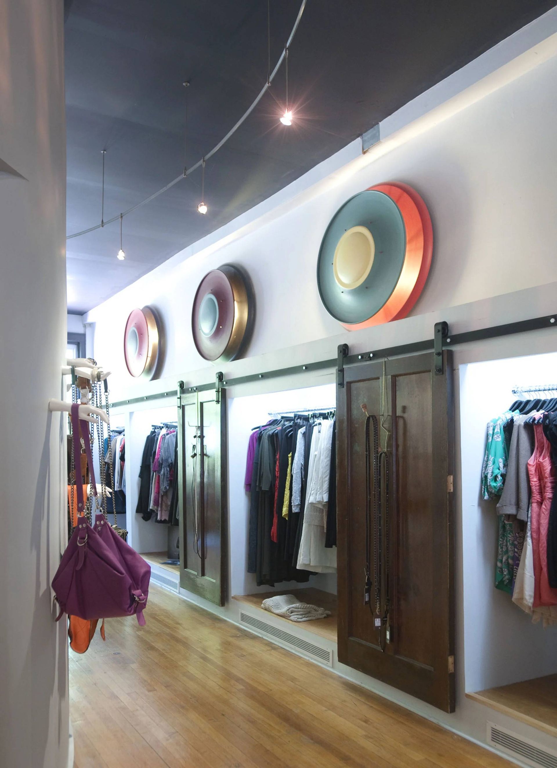 Clothing store interior with racks of clothes, wooden doors, and colorful circular wall decor.