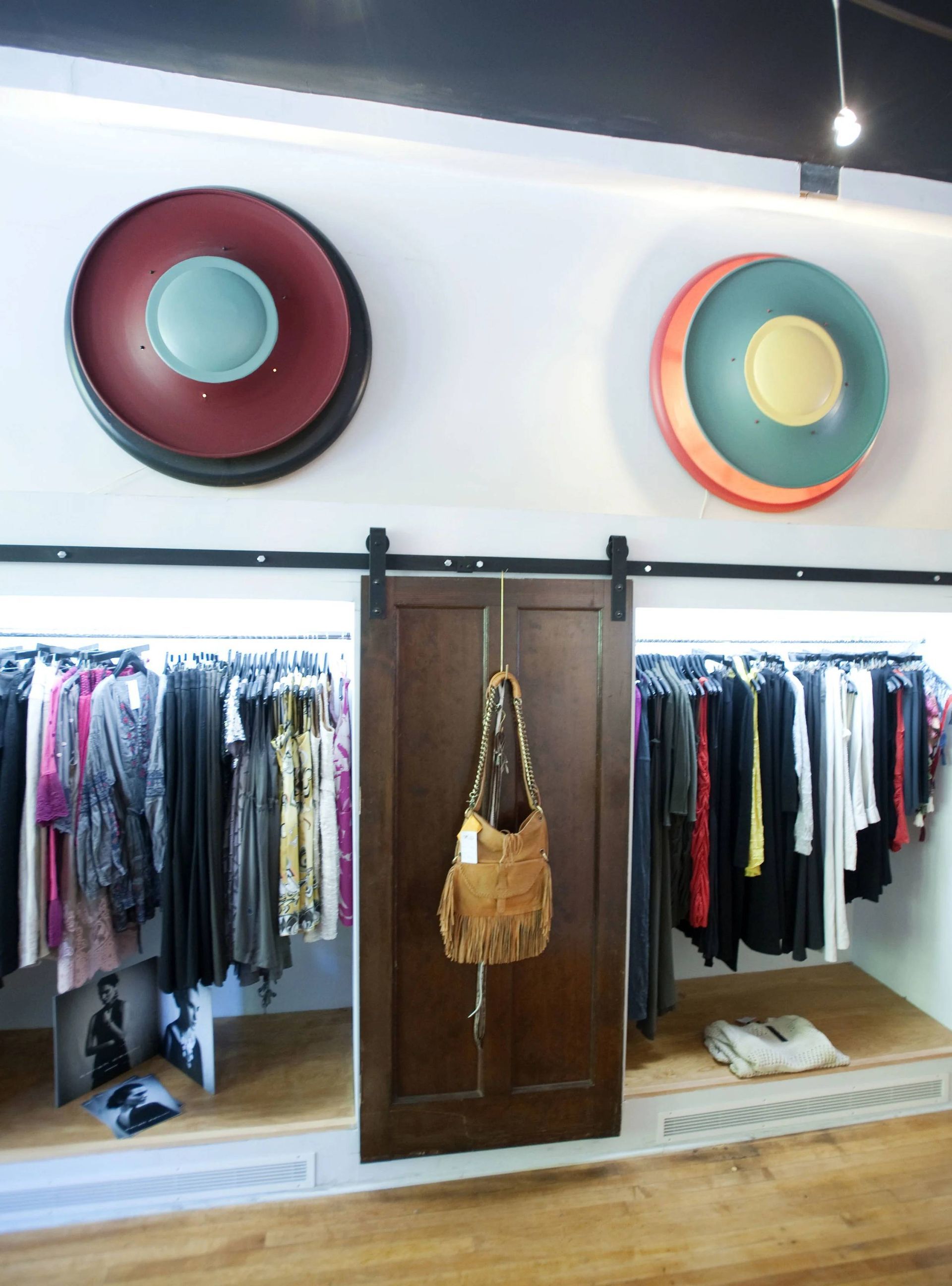 Boutique clothing rack with hanging clothes, wooden cabinet, and colorful wall hats above