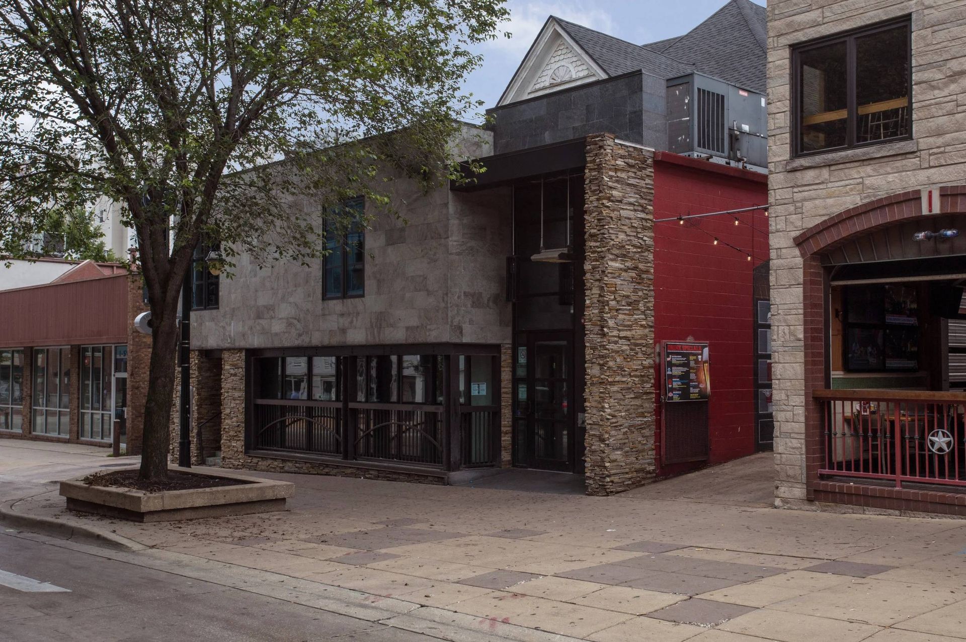 Quiet street with modern storefronts, brick facades, and a tree-lined sidewalk