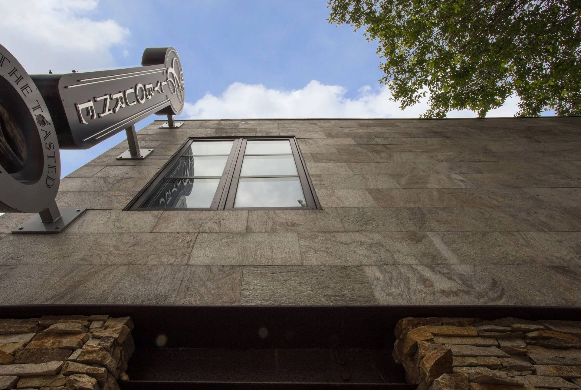 Low-angle view of a stone building facade with windows and a metal sign against a blue sky