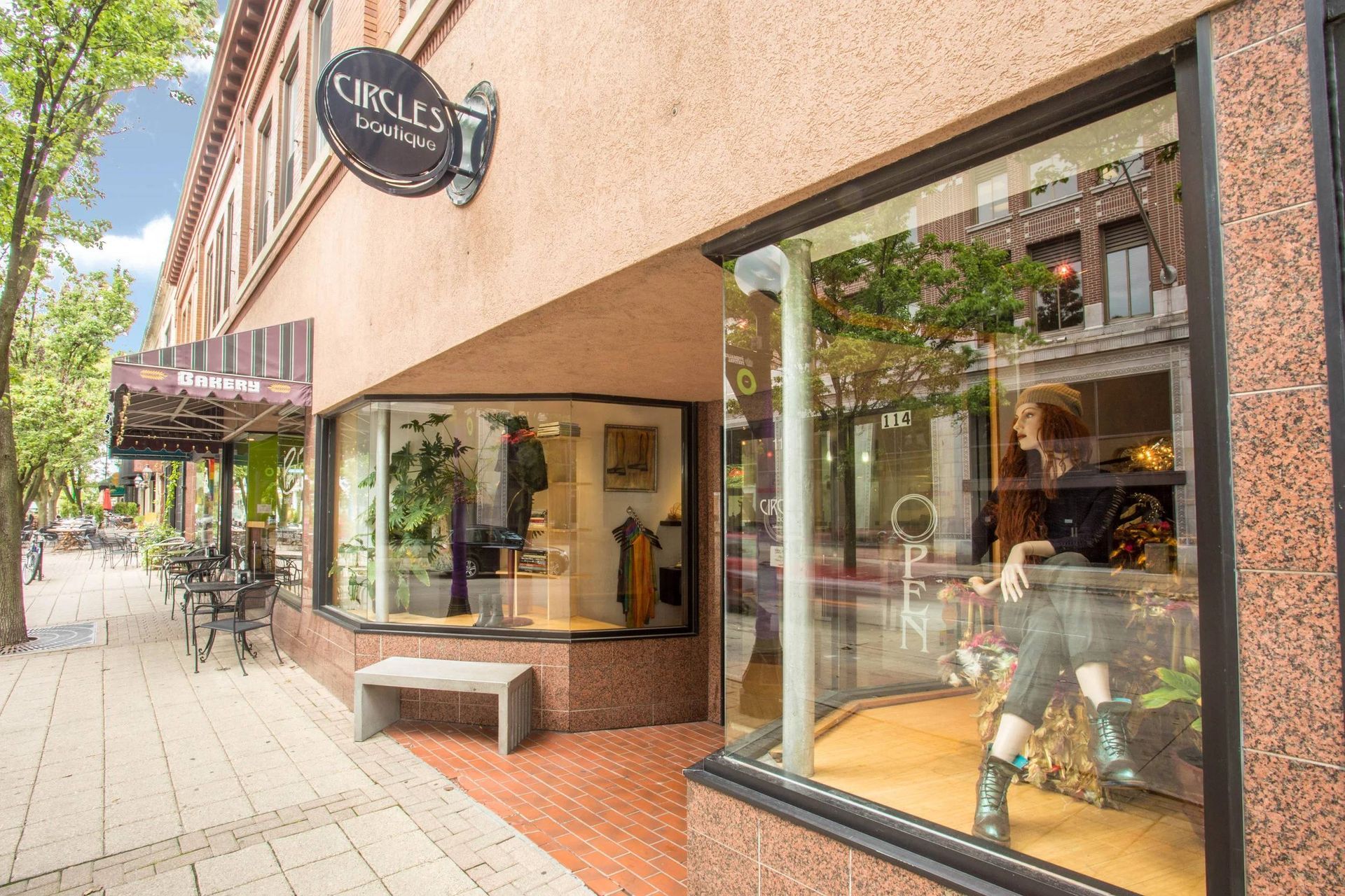 Storefront with large windows and a sidewalk bench on a tree-lined street