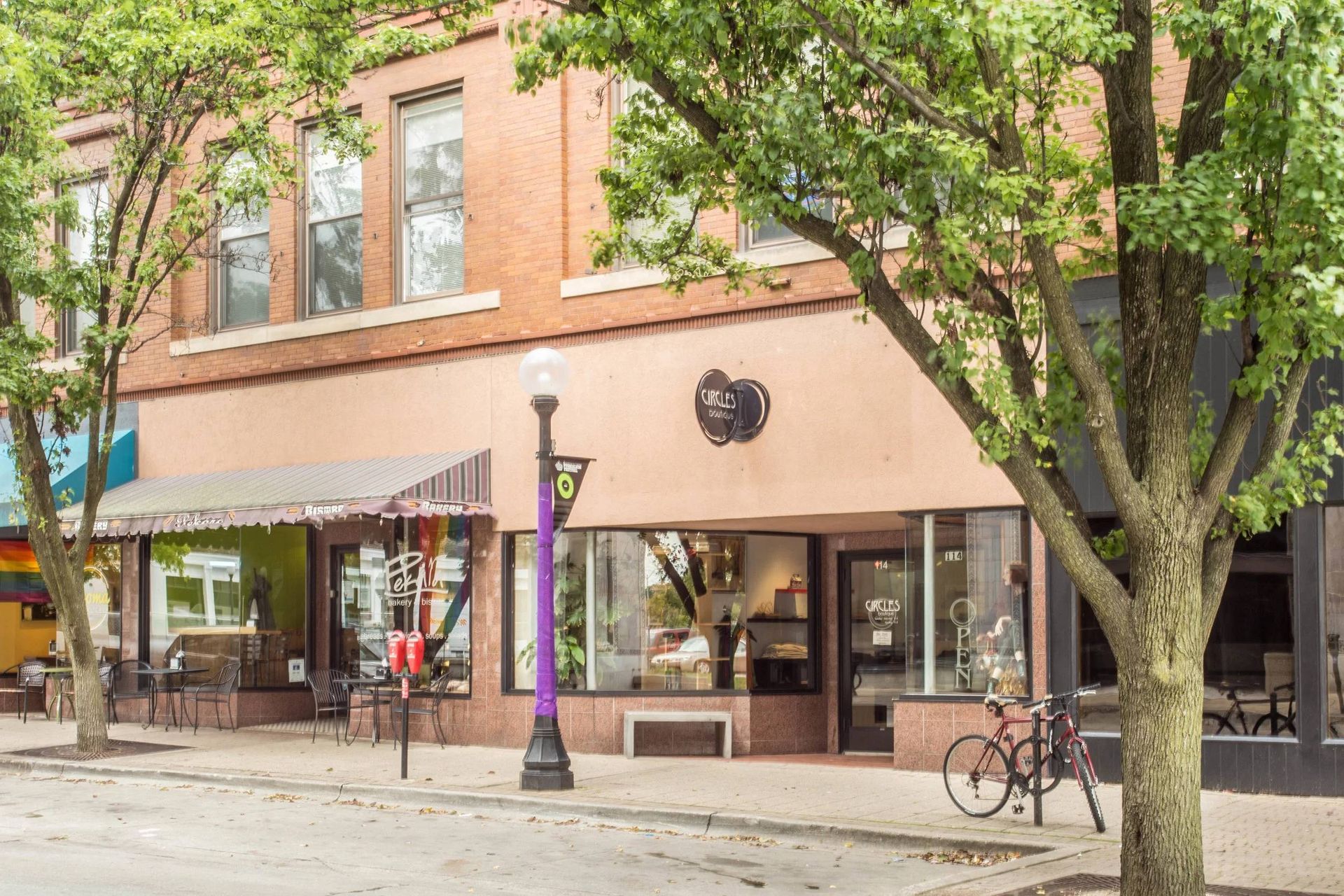 Tree-lined street with brick storefronts, outdoor seating, and a bicycle parked by the sidewalk.