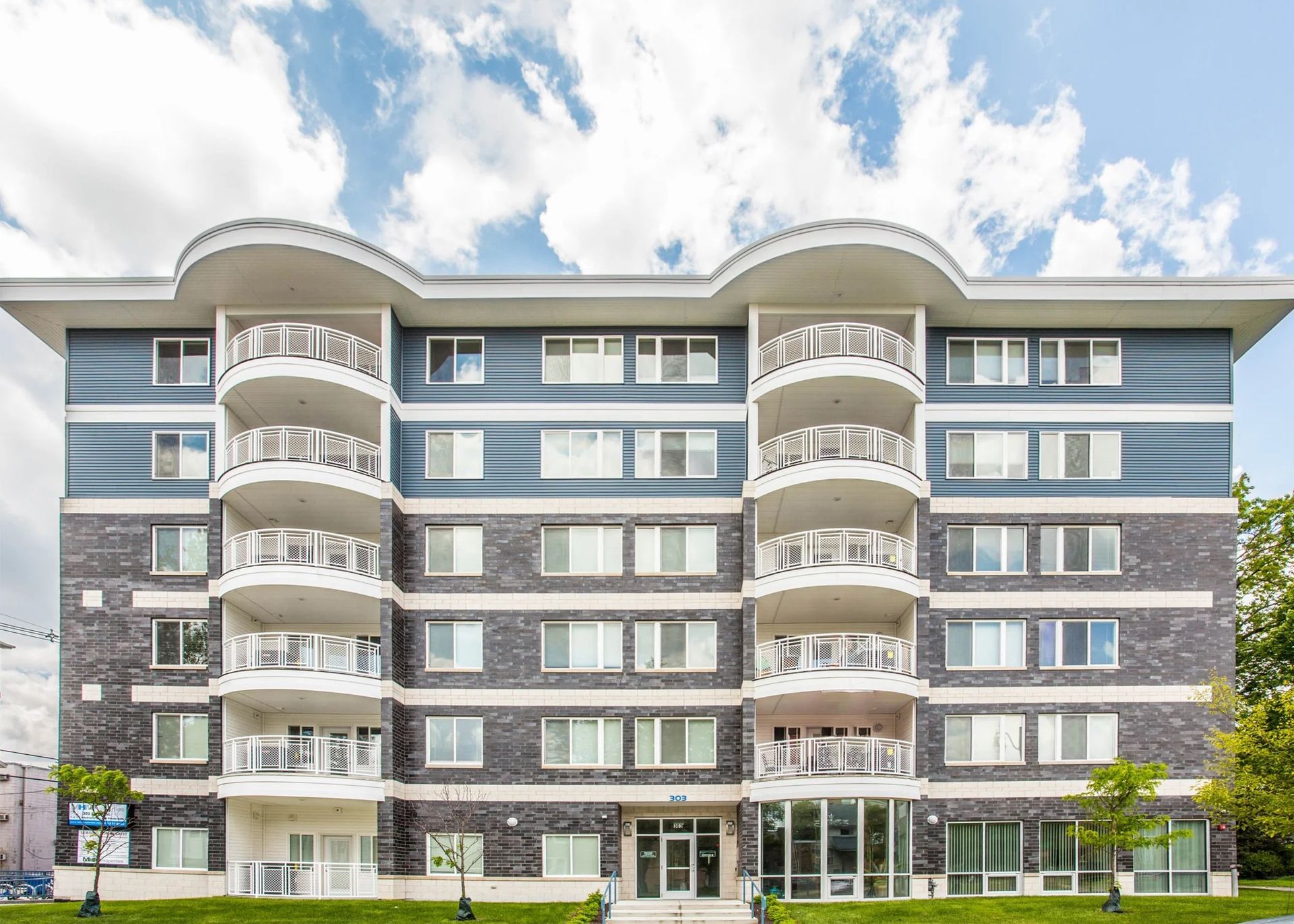 Modern gray-and-white apartment building with balconies and large windows under a cloudy sky