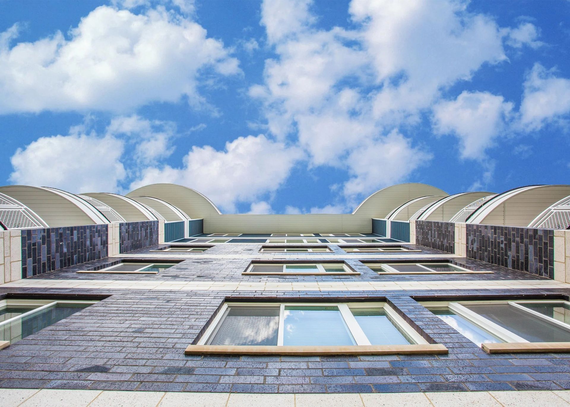 Low-angle view of a modern stone building with arched rooftops against a blue, cloudy sky