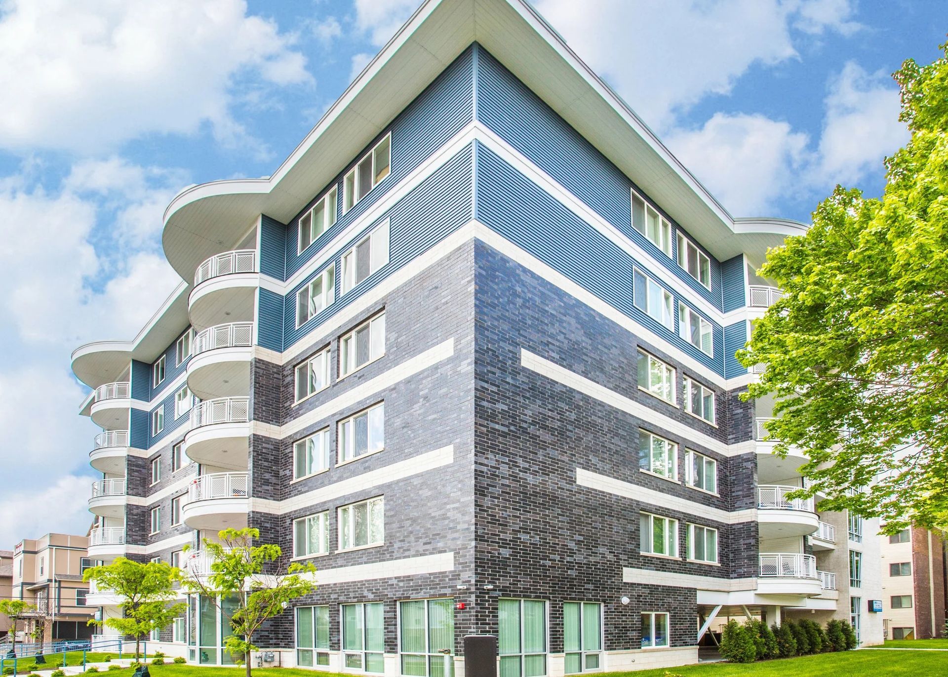 Modern multi-story apartment building with blue-gray facade and white balconies under a bright sky.