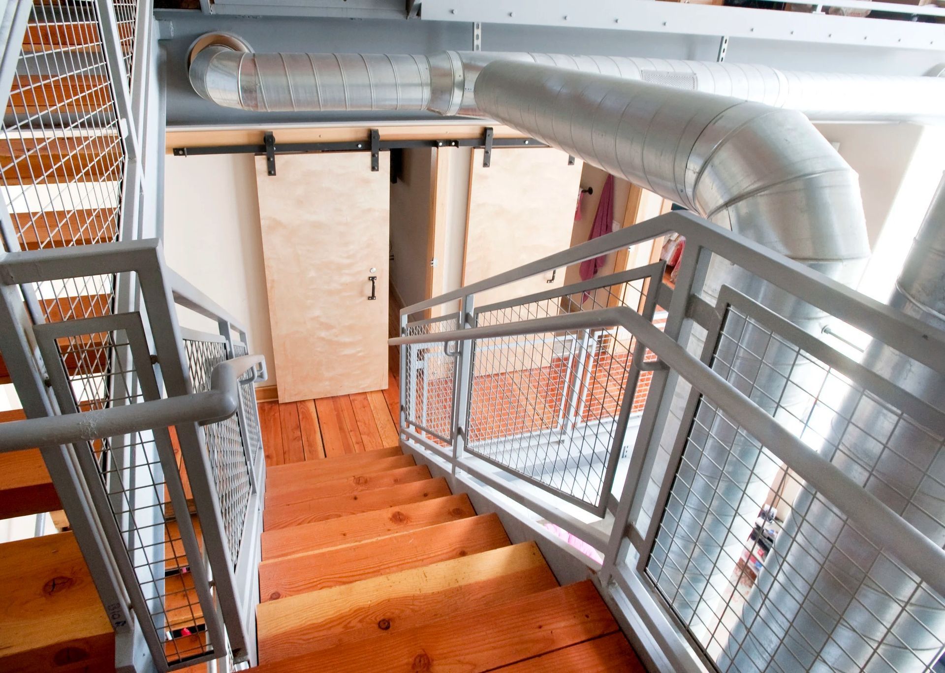 Interior stairwell with orange wooden steps, metal railings, and exposed ductwork overhead.