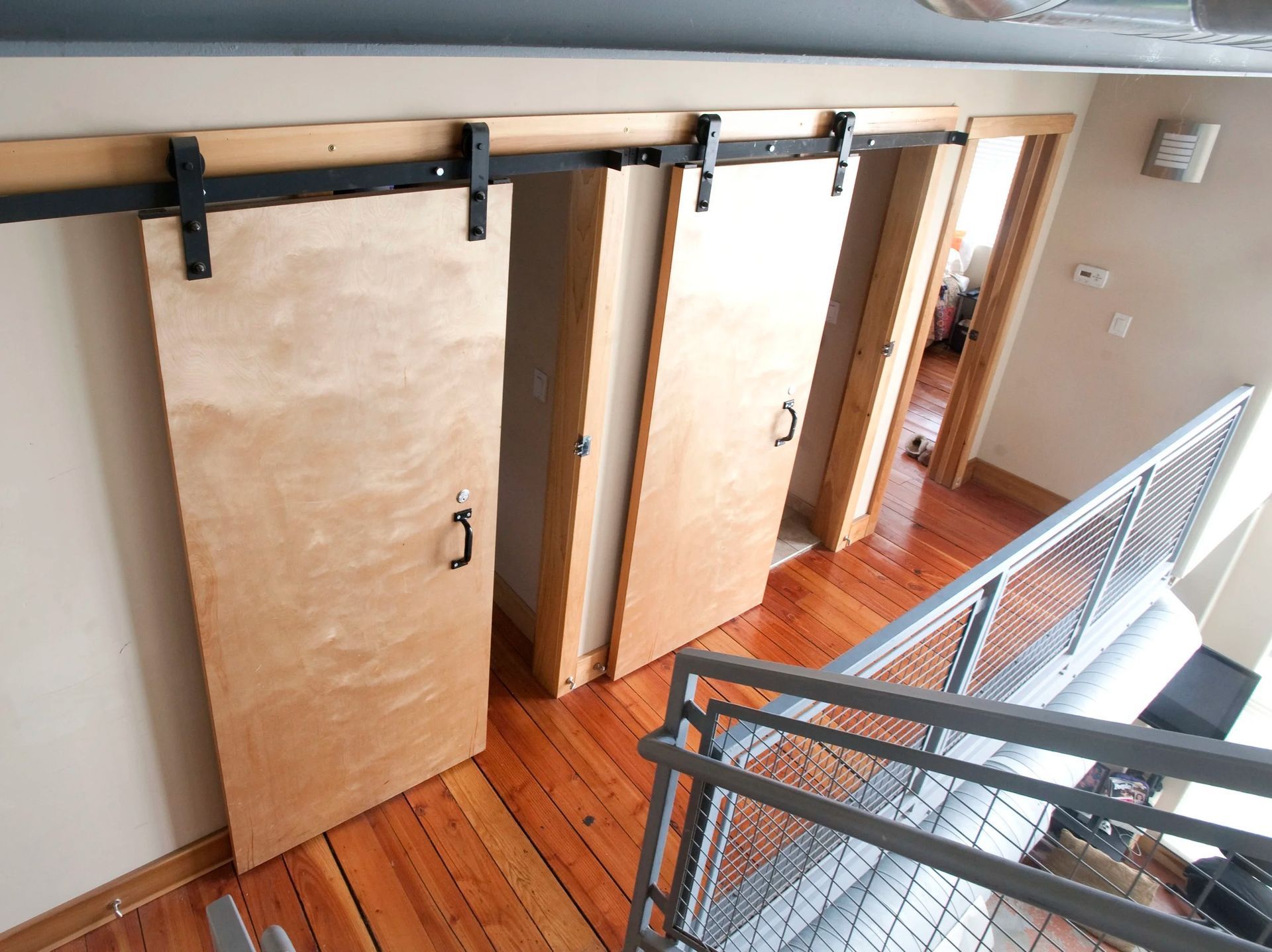 Three closed wooden sliding doors with black hardware along an upper-floor hallway by a railing