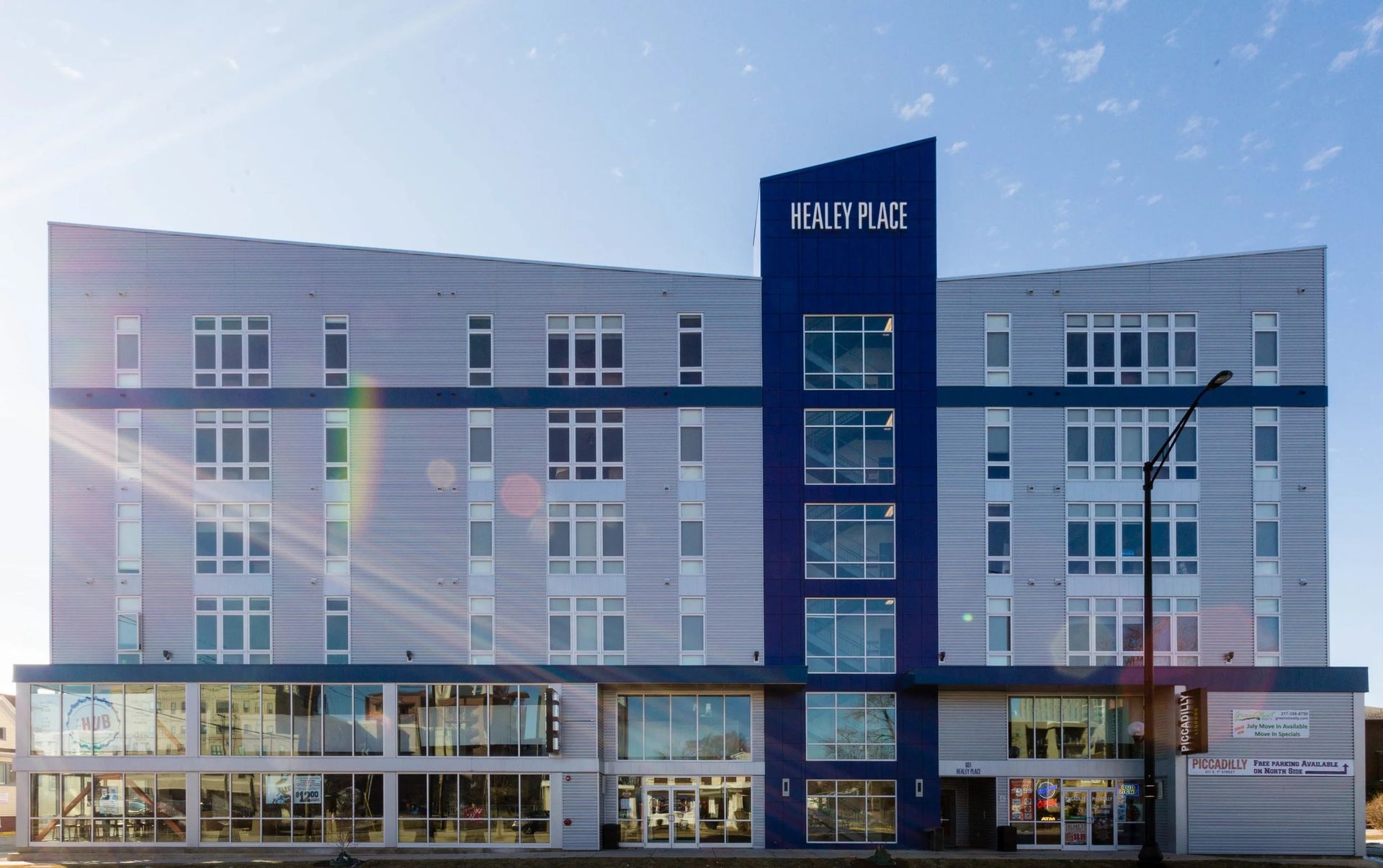 Modern multi-story apartment building with a blue central tower and ground-floor storefronts