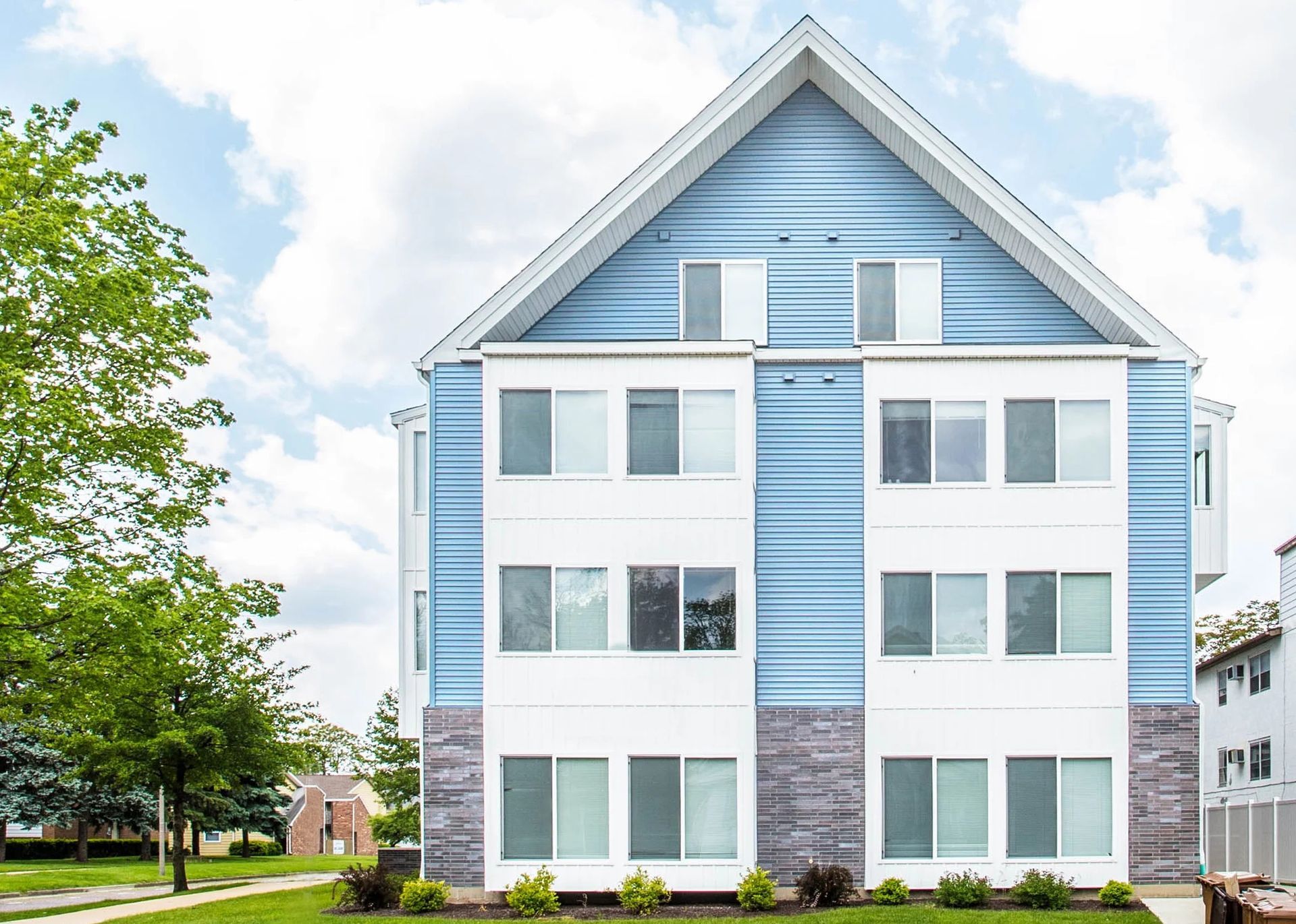 White multi-story apartment building with blue vertical siding and a peaked roof under a partly cloudy sky