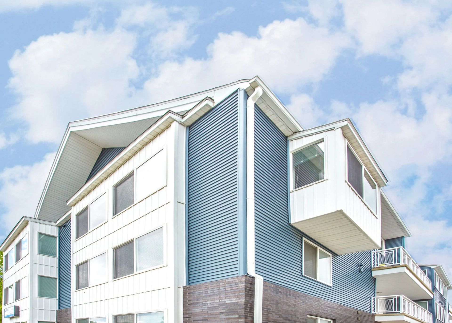 Modern white apartment building with blue siding and balconies under a bright sky
