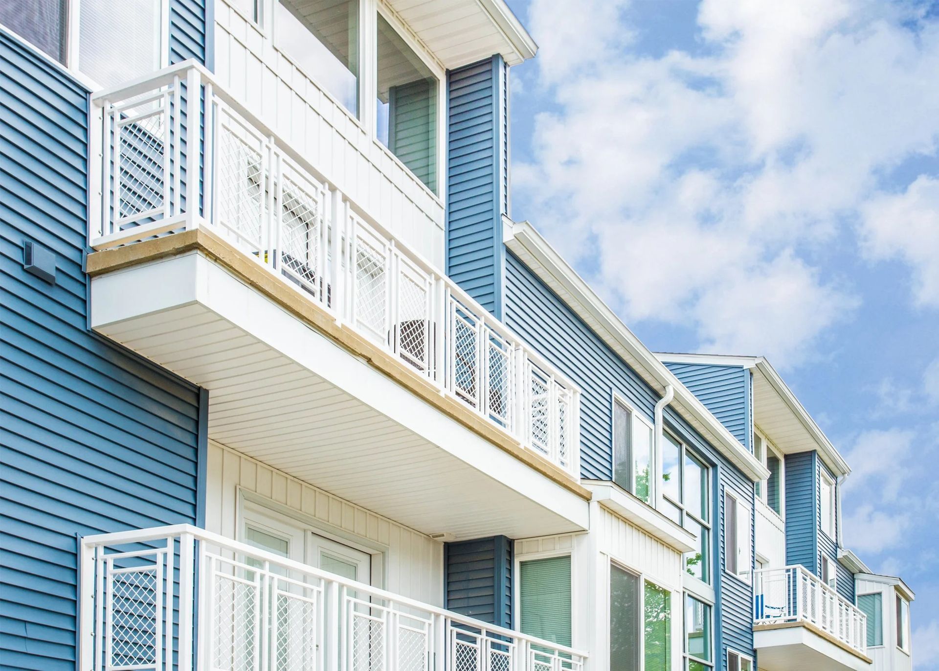 Blue coastal apartment building with white balconies against a partly cloudy sky