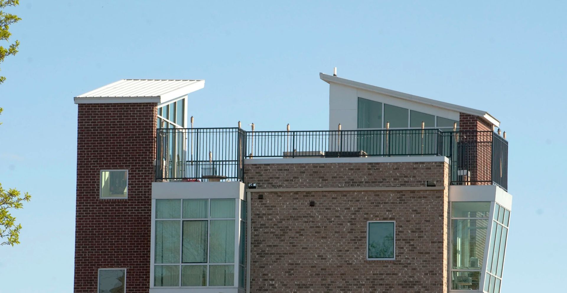 Modern brick building with rooftop terrace and white slanted roof against a blue sky