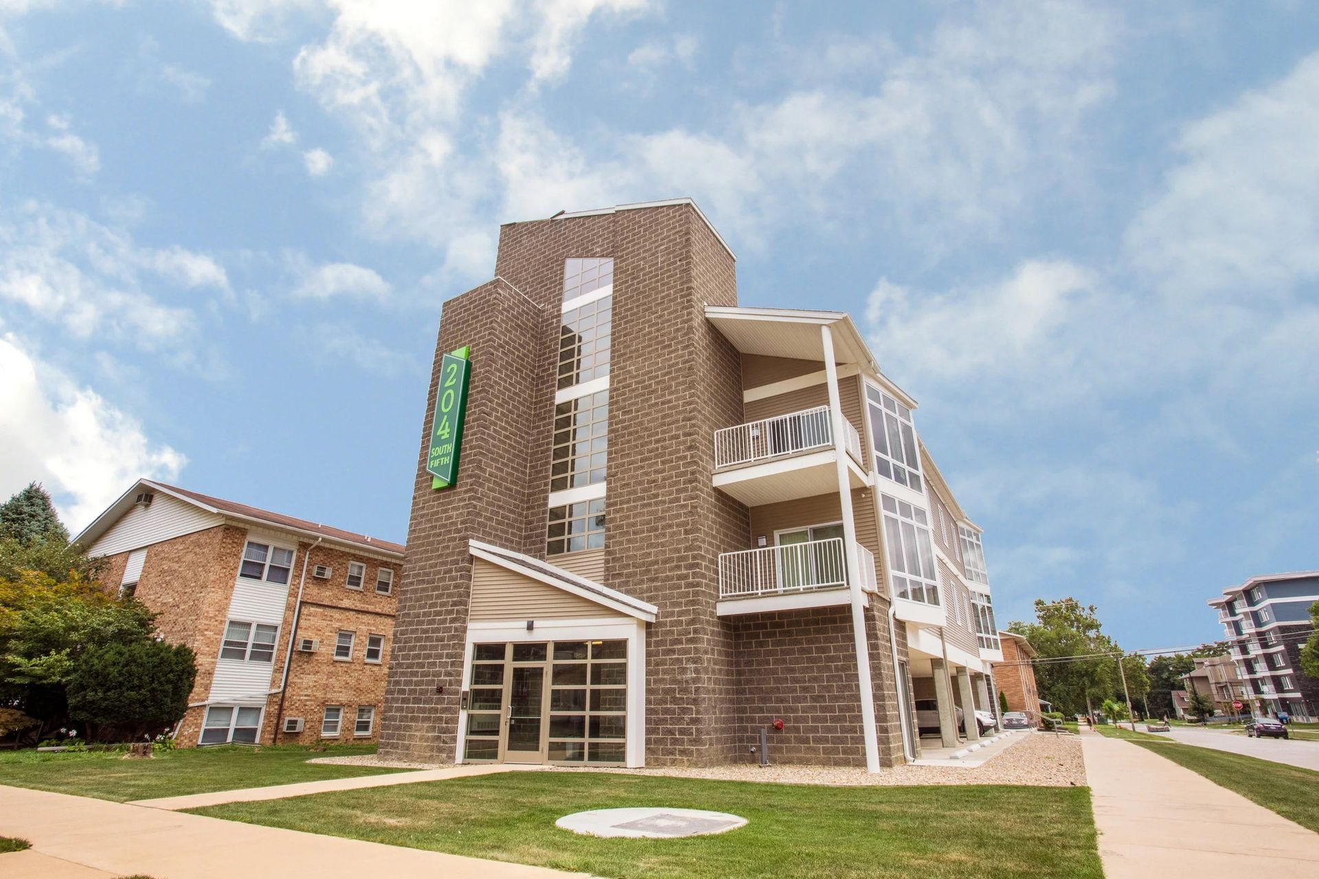 Modern brick dormitory building with balconies and a grassy courtyard under a blue sky