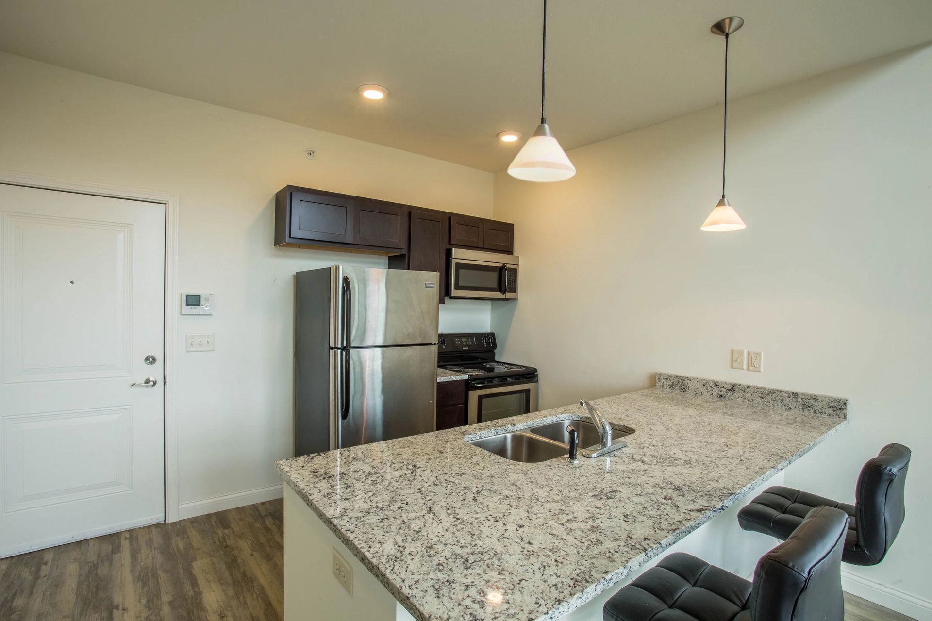 Modern kitchen with granite island, stainless steel appliances, pendant lights, and barstools